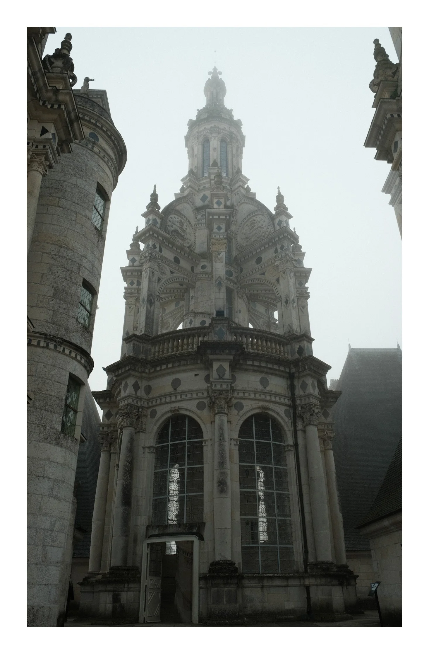 A historic church with ornate stone architecture, large stained glass windows, and a prominent central tower, shrouded in fog.
