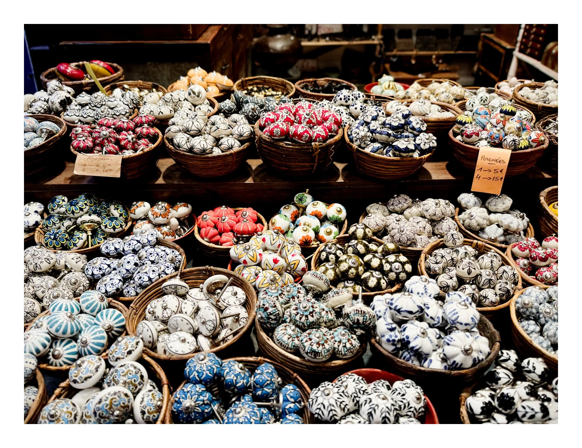 Baskets of colorful and patterned ceramic knobs and drawer pulls on display at a market stall.
