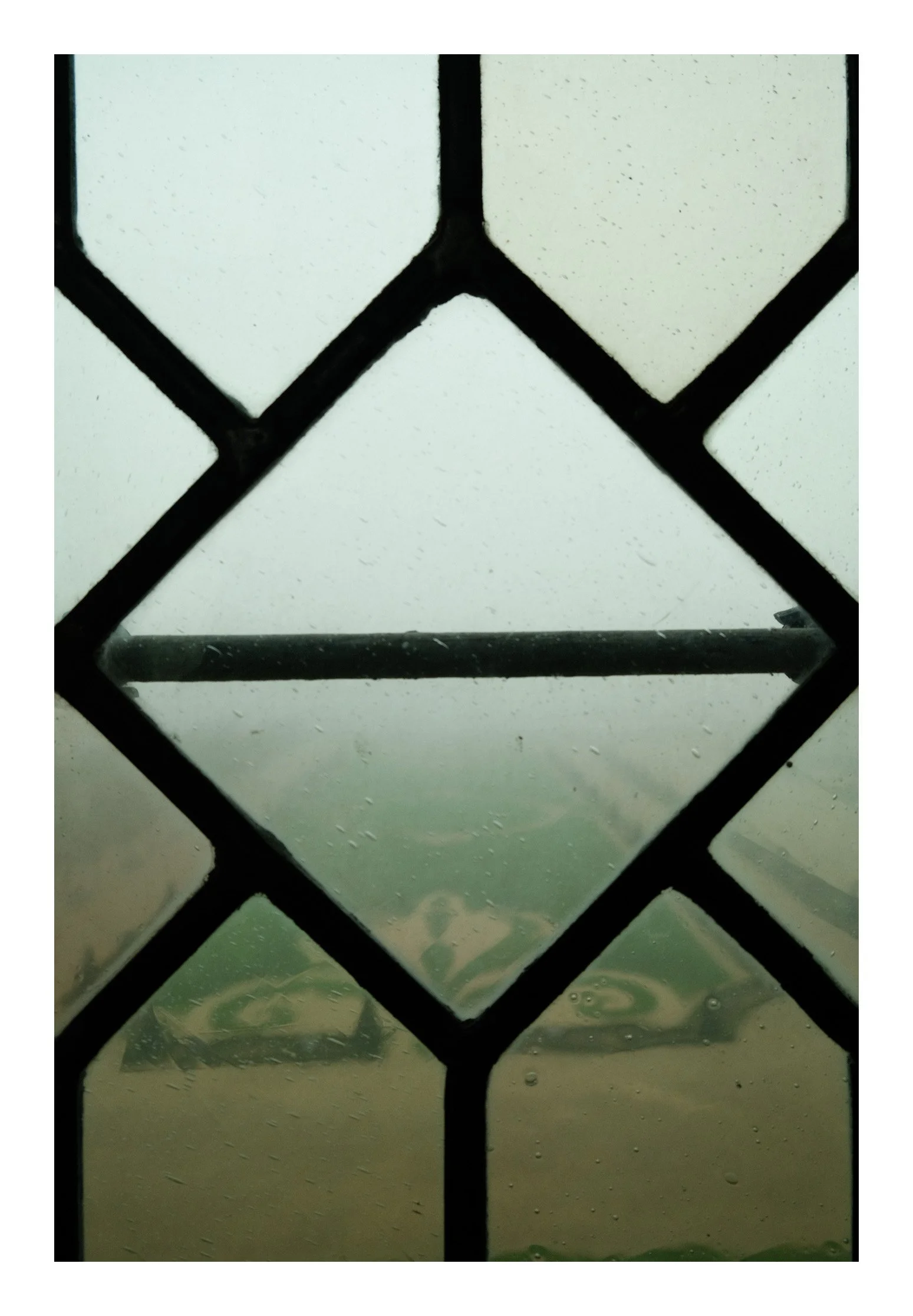 View through a rain-covered window with a diamond-shaped lattice pattern.