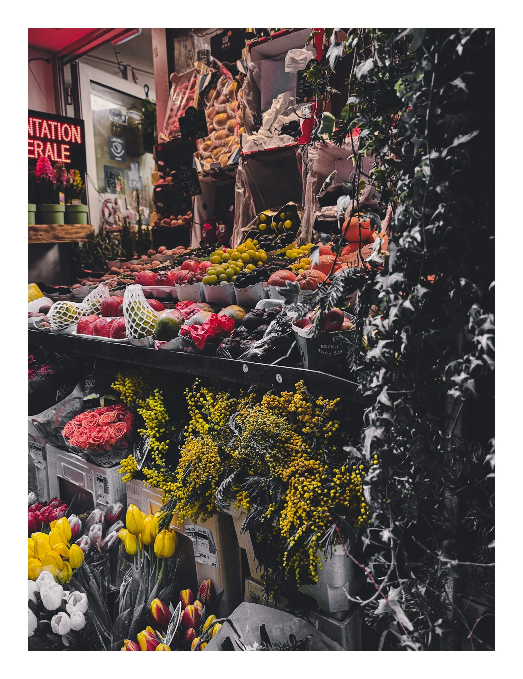 Display of various fresh fruits and colorful flowers at a market stall, including apples, grapes, tulips, and yellow blossoms.