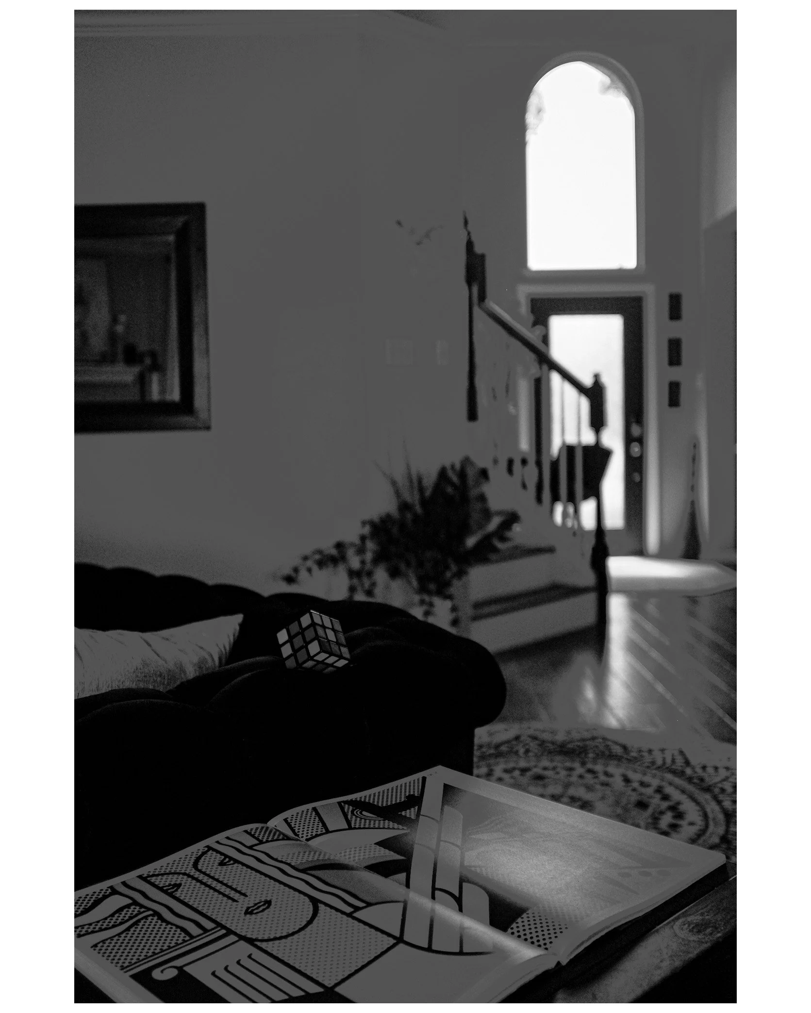 Living room with open door, staircase, window, a Rubik's Cube on a couch, and an open magazine on a table.