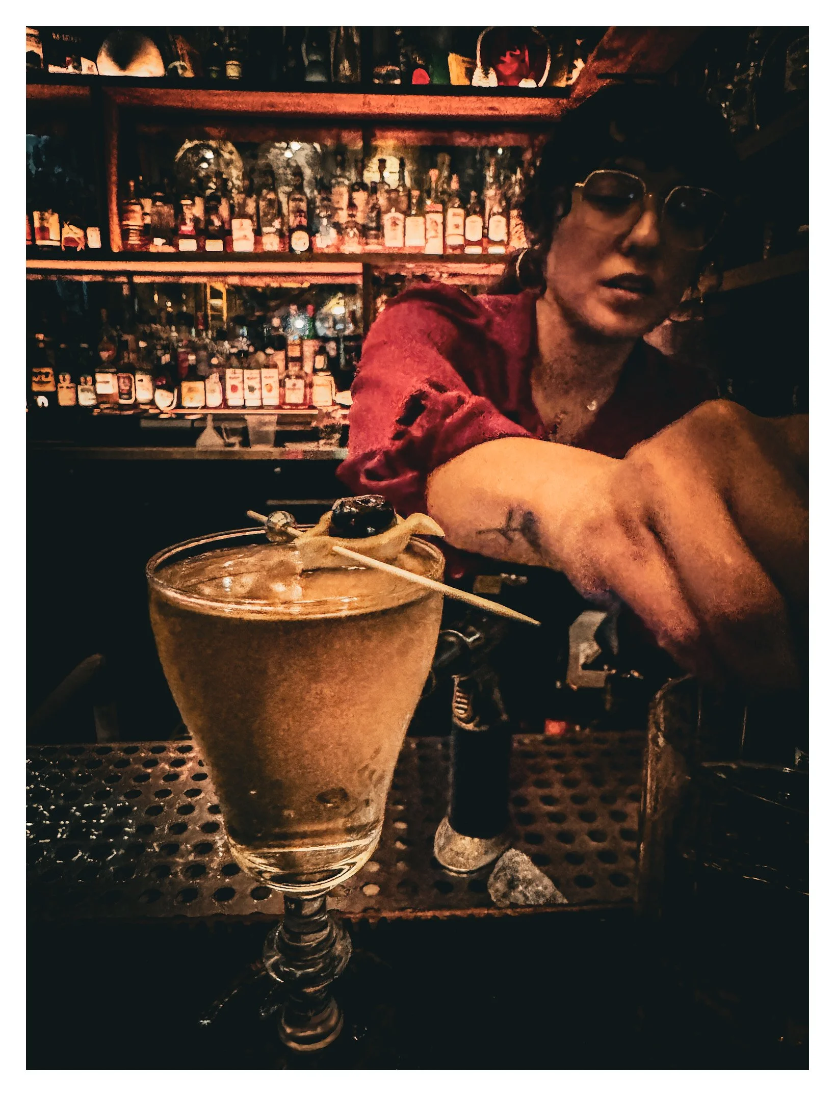 A bartender preparing a drink behind the bar with liquor bottles on shelves in the background.