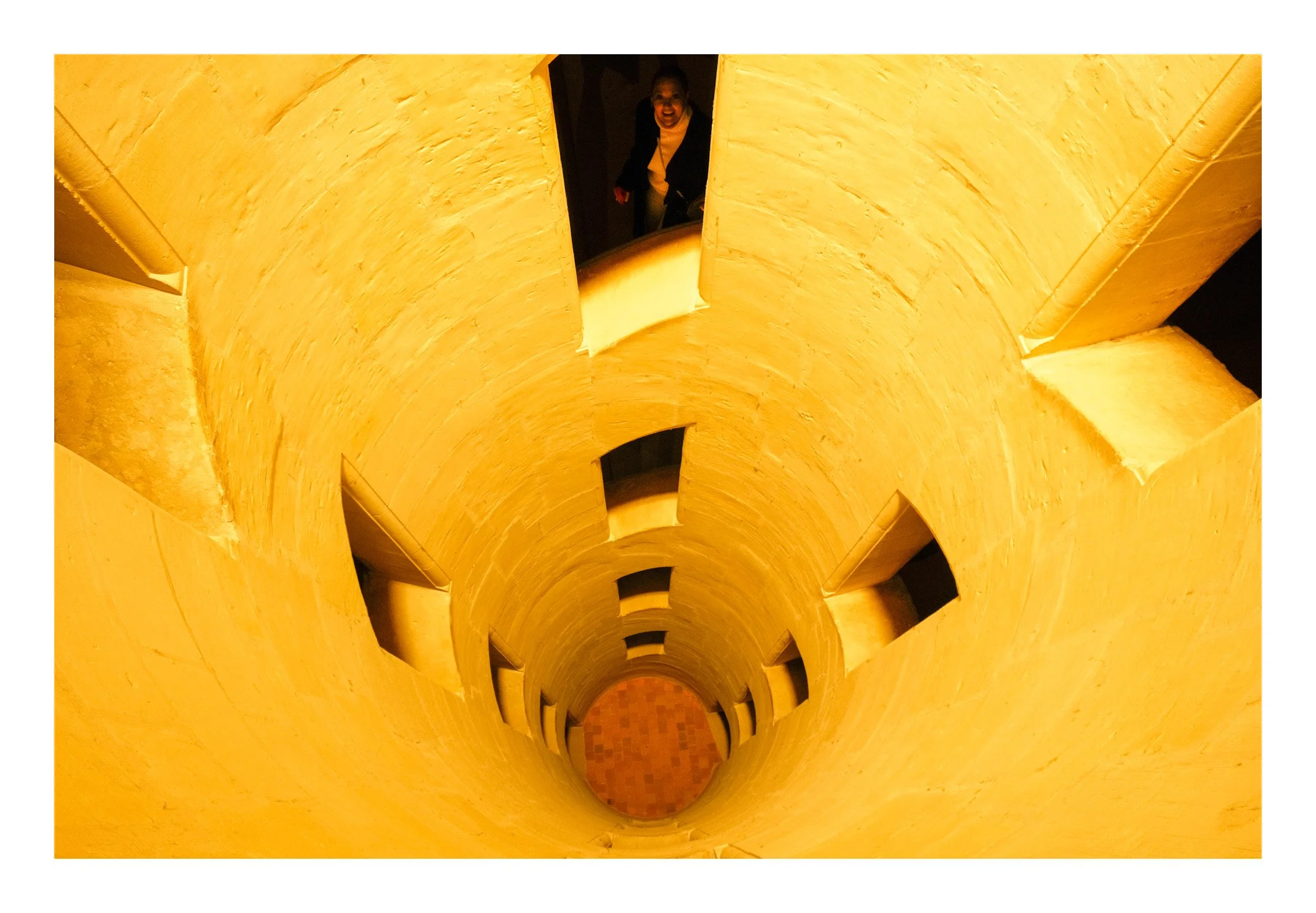 A woman is looking down a yellow spiral staircase with square openings in the center.