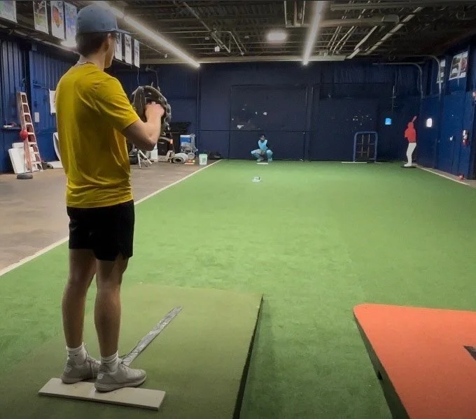Indoor baseball practice with person pitching on artificial turf