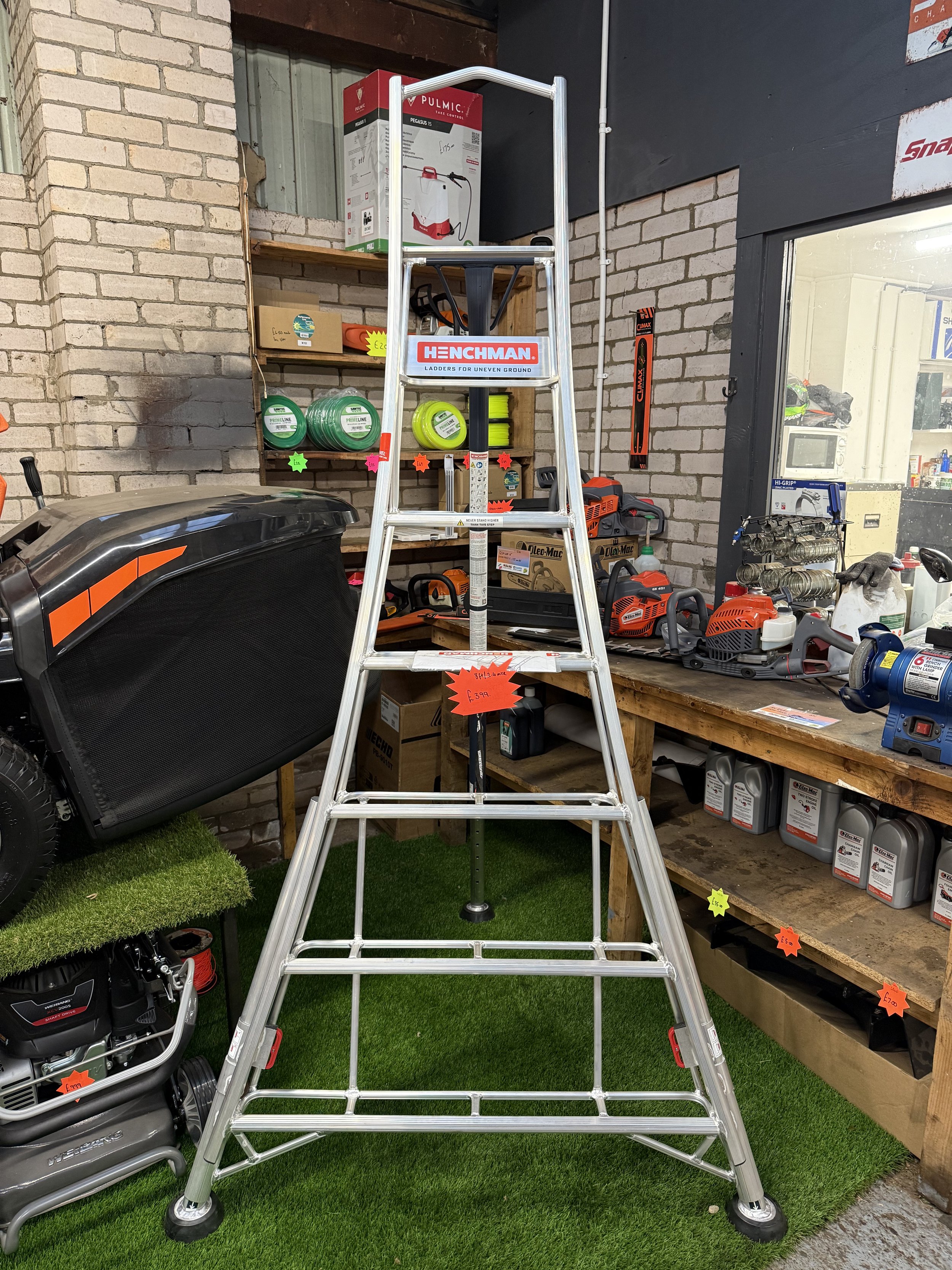 A silver aluminum step ladder in a hardware store, surrounded by tools and equipment, with a brick wall and shelves in the background.