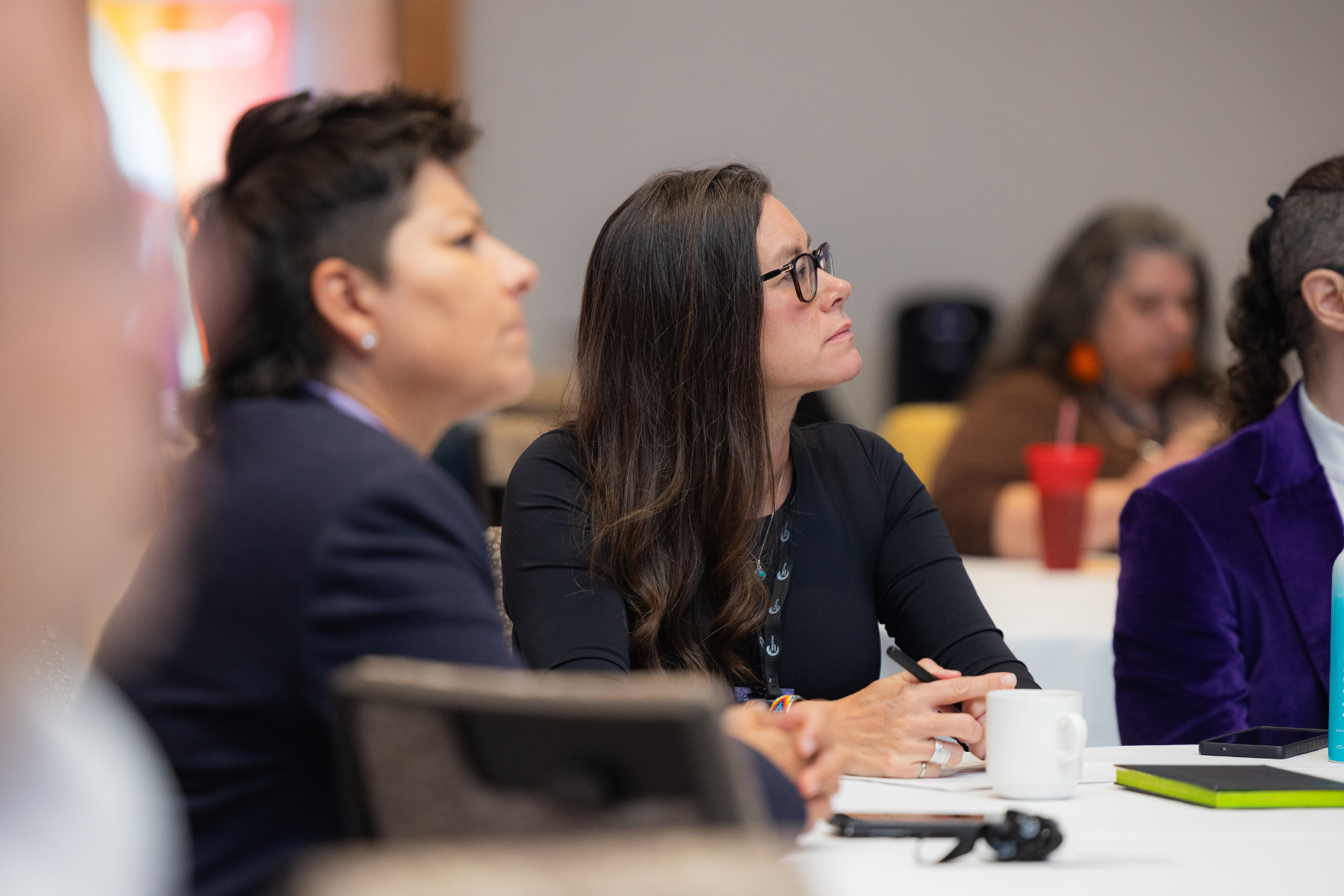 Women sitting at a table attentively listening during a conference or meeting.