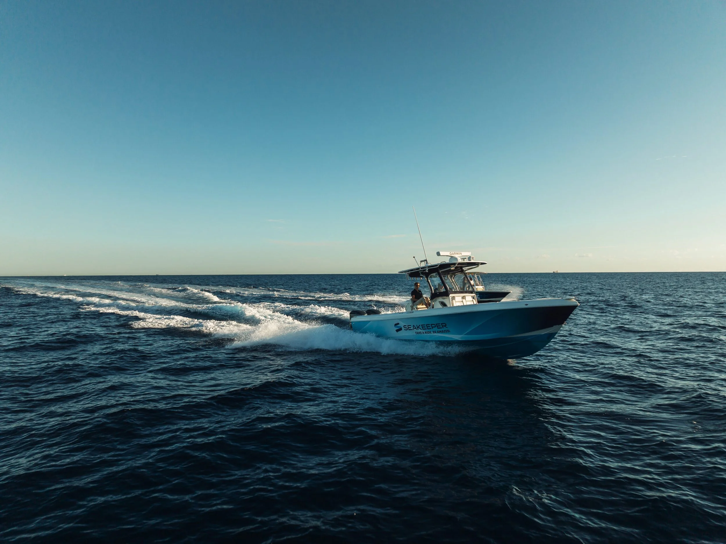 A sleek blue and white speedboat named 'Seakeeper' speeding across calm ocean waters during sunset, leaving a trail of white foam behind.