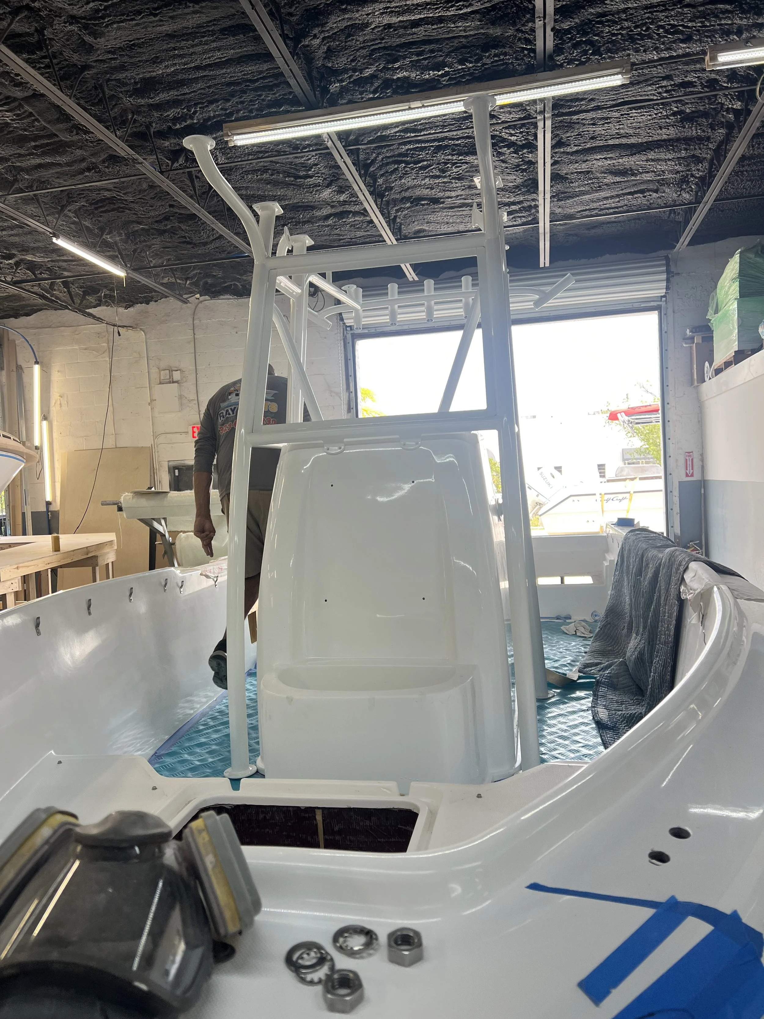 White boat under construction inside a workshop, with a person working on it, and tools and parts visible around.