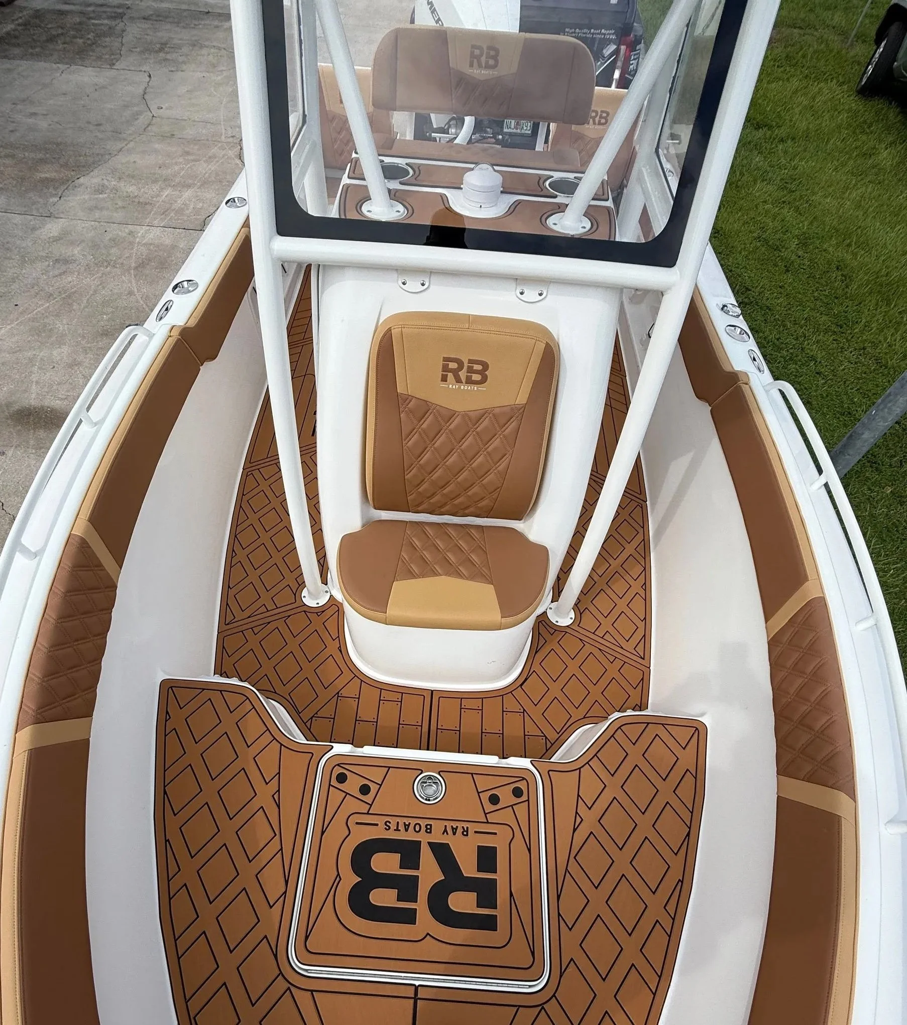 View from above of the interior of a small Ray Boats RB3 boat, featuring a tan and brown cushioned seat with the RB logo, a transparent windshield, and brown patterned flooring.