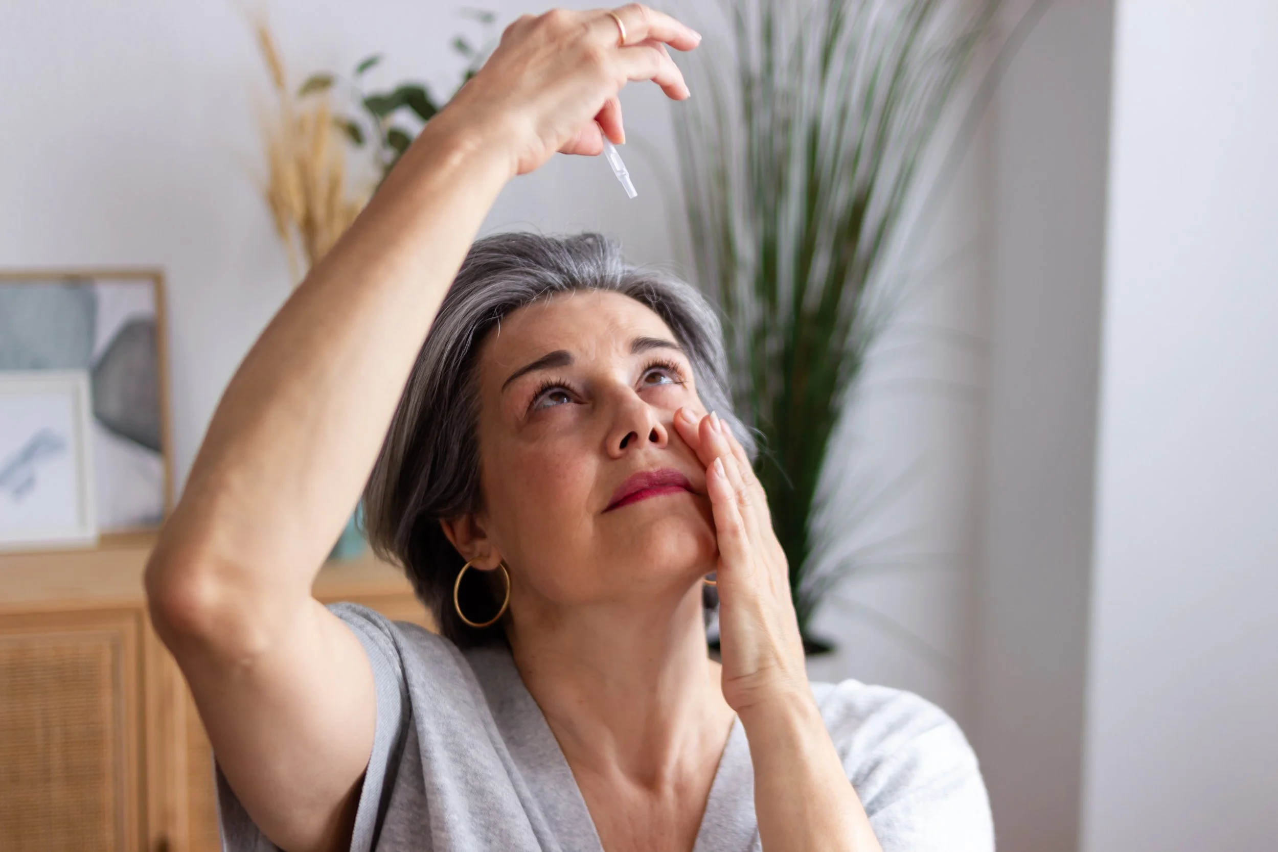 An older woman with artificial tears trying to help her dry eye disease.