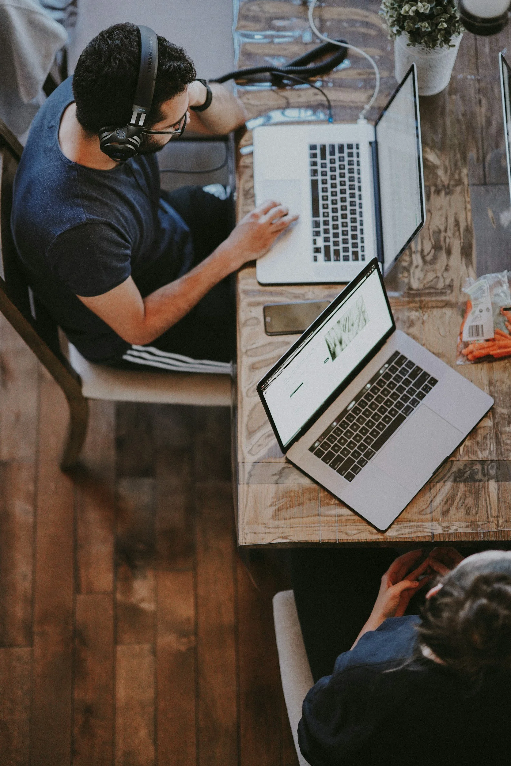 Two people working at a wooden table on laptops, one wearing headphones.
Human resources consulting. 
HR