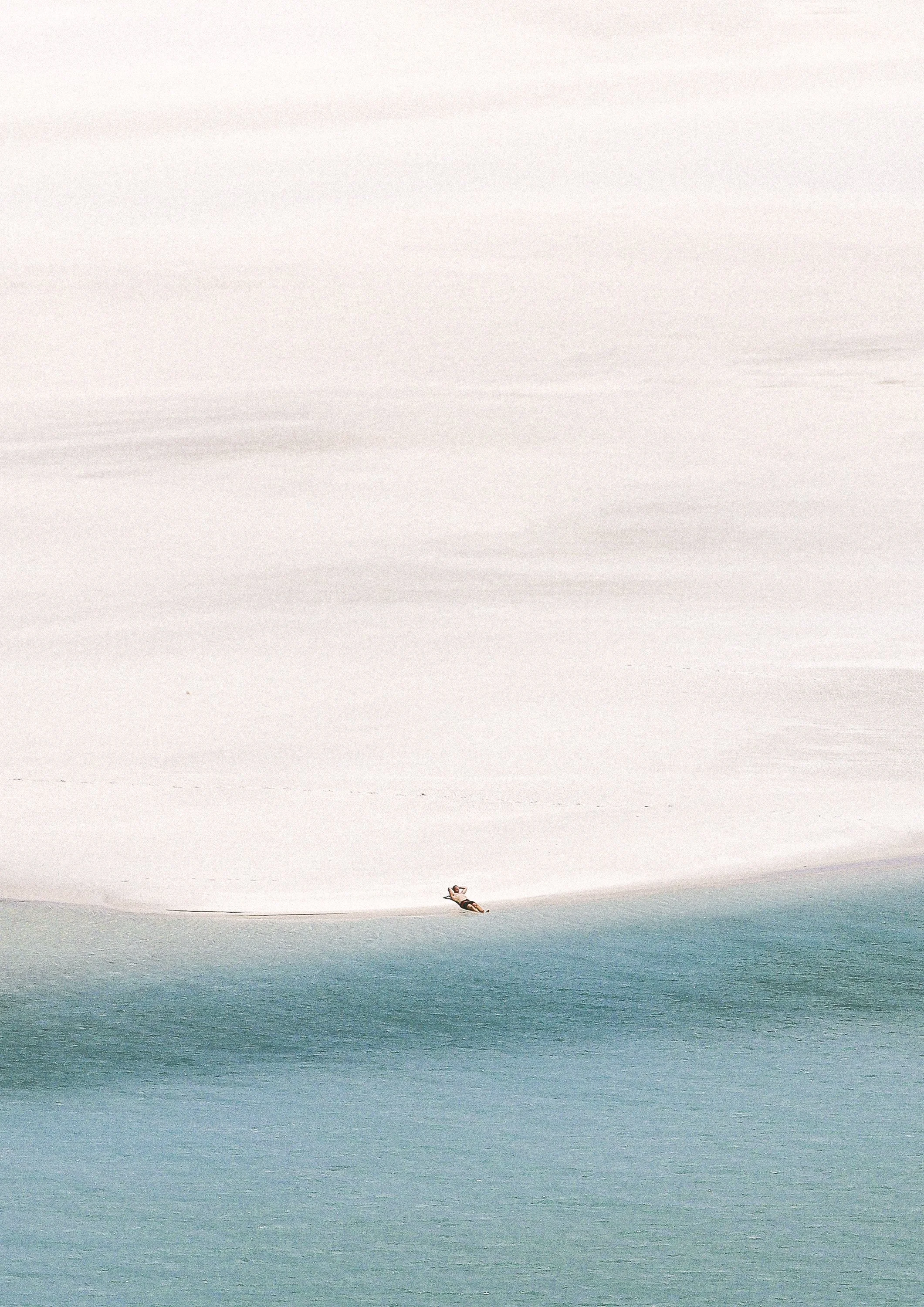 A man laying on a vast beach with ocean
