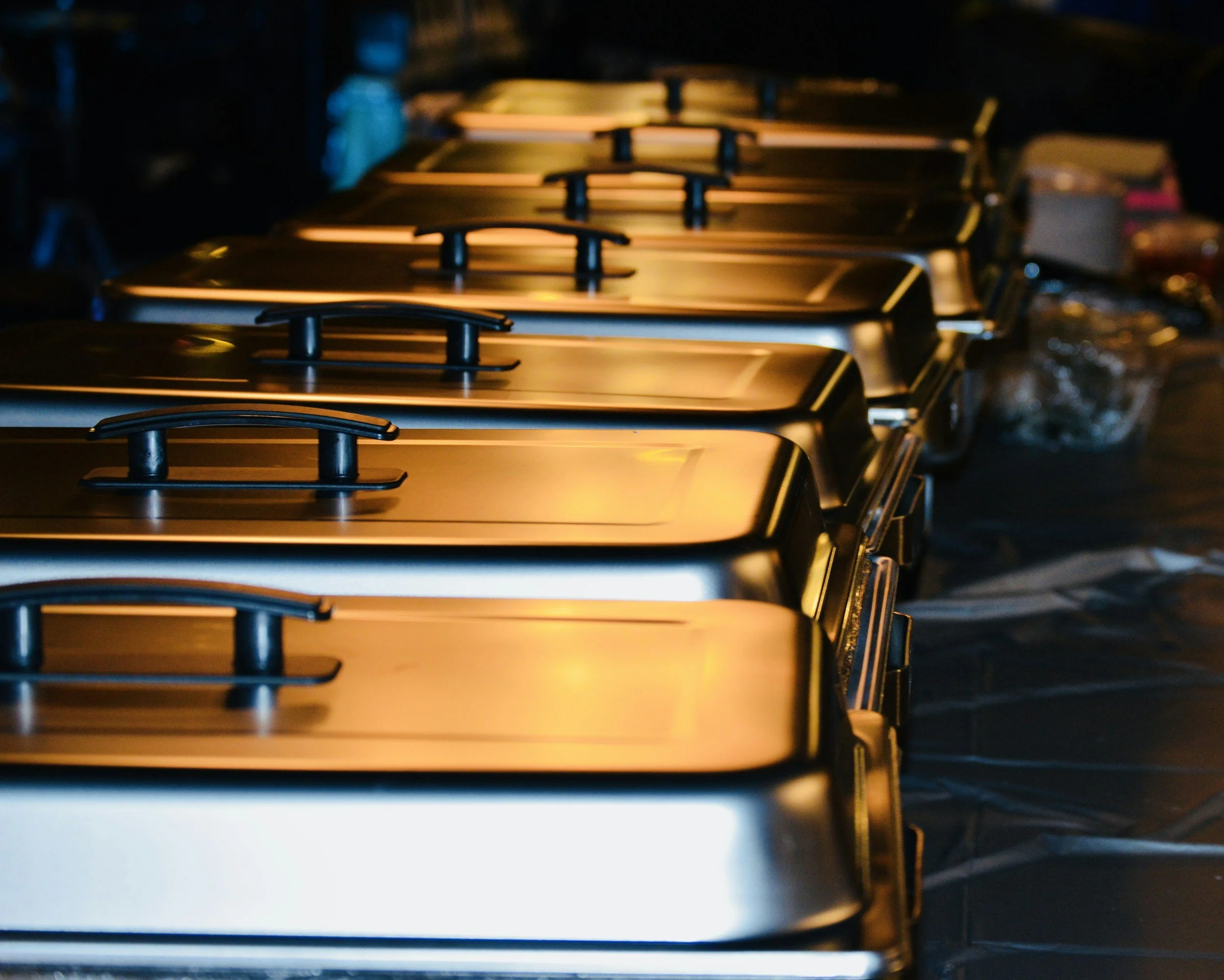 Multiple stainless steel gas stove burners with black knobs, reflecting warm light in a dark kitchen setting.