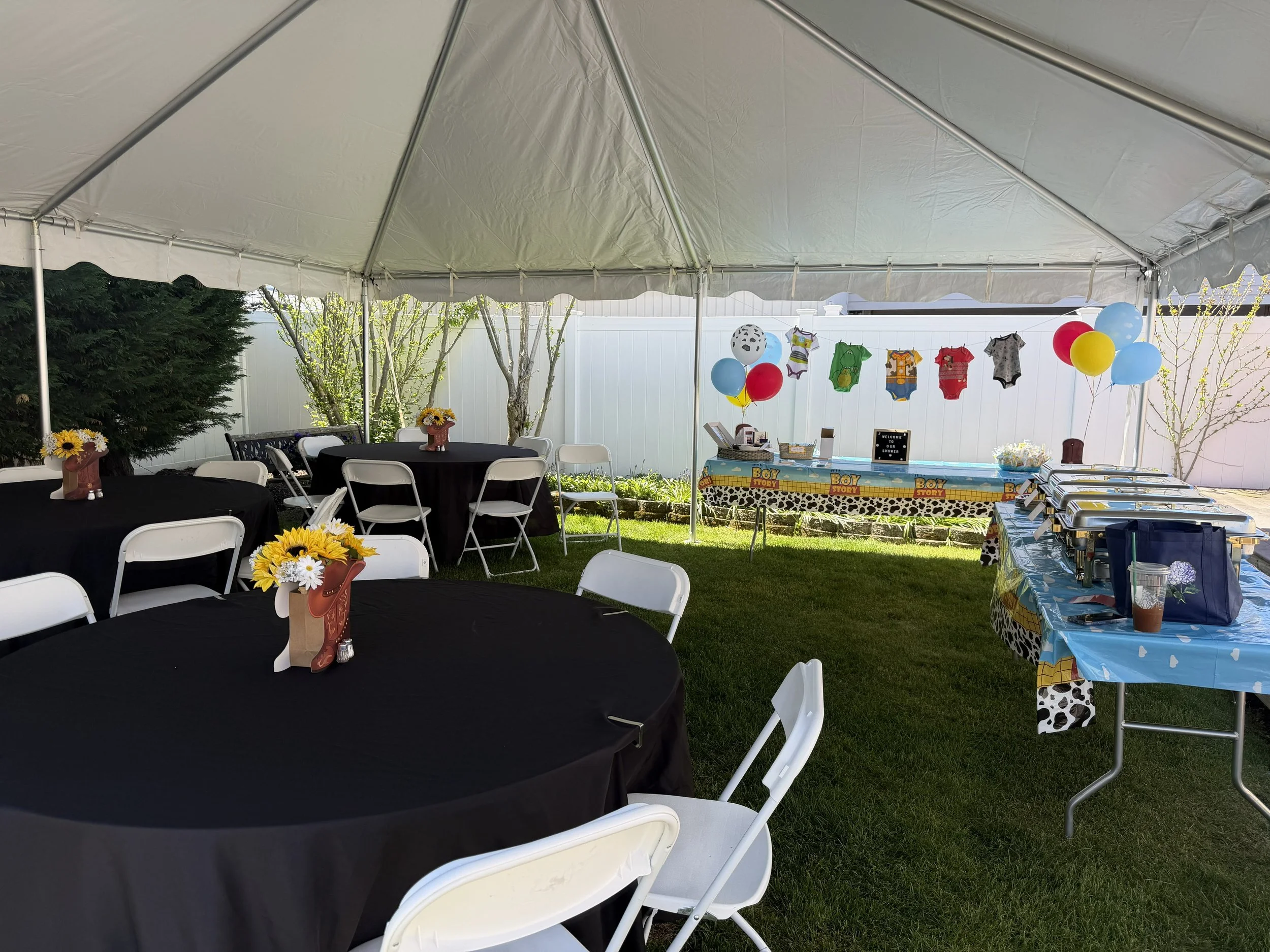 Outdoor birthday party setup under a white tent with black and blue themed decorations, tables with black and blue tablecloths, balloon arrangements, and a children's themed birthday cake table.