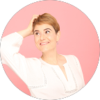 A woman with short blonde hair, wearing a white cardigan, smiling and looking upward against a pink background.