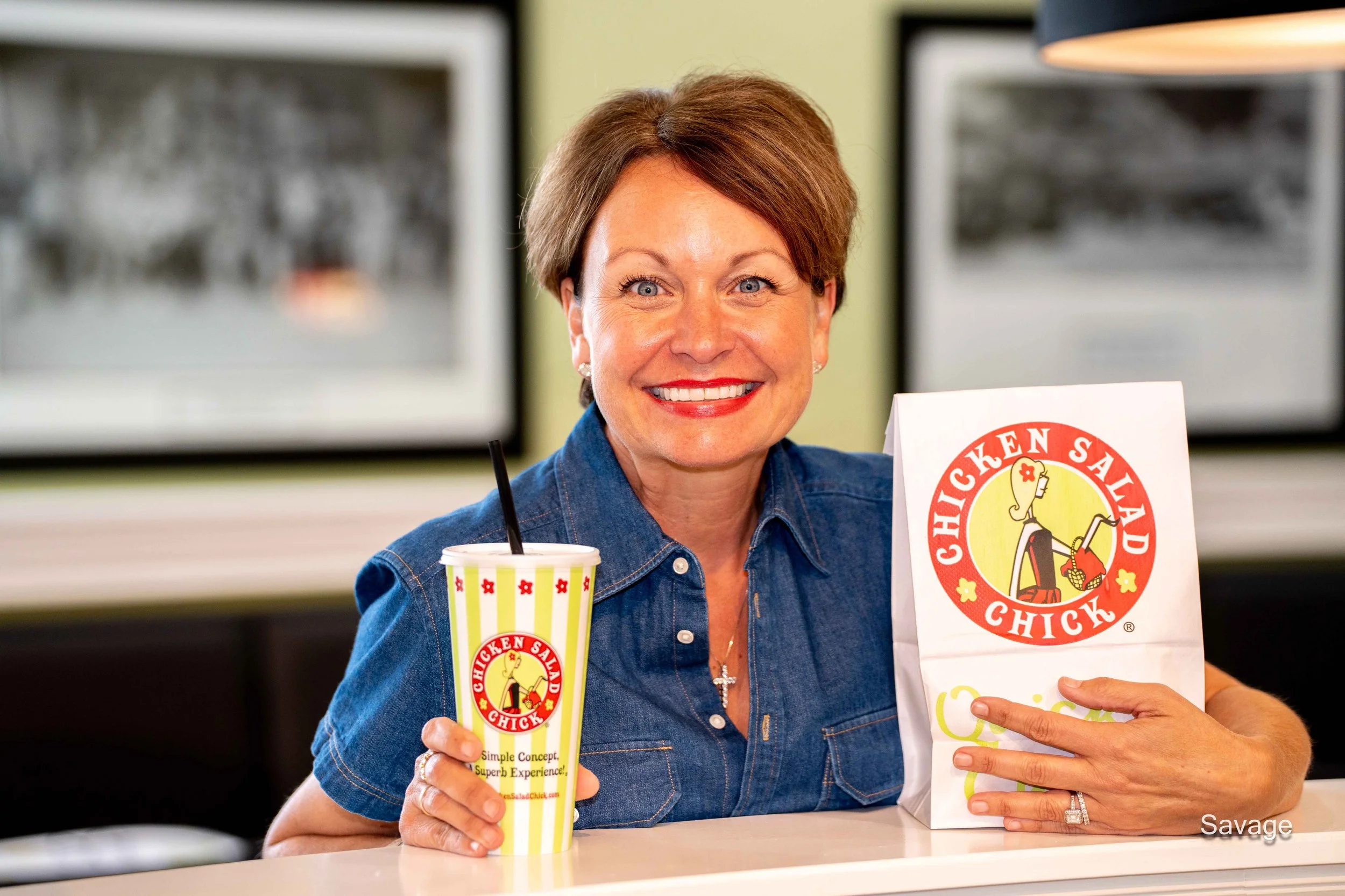 A person holding a Chicken Salad Chick cup and a paper bag with the brand's logo.