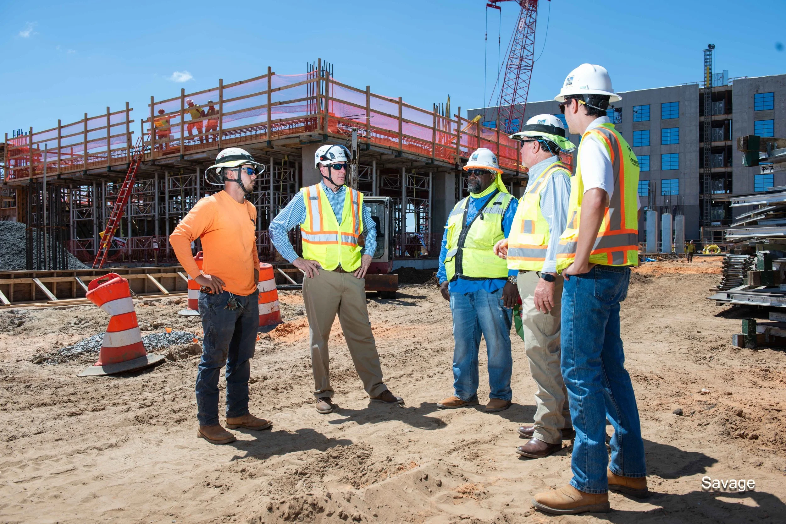 Construction workers in safety gear discussing at a building site with cranes and scaffolding.