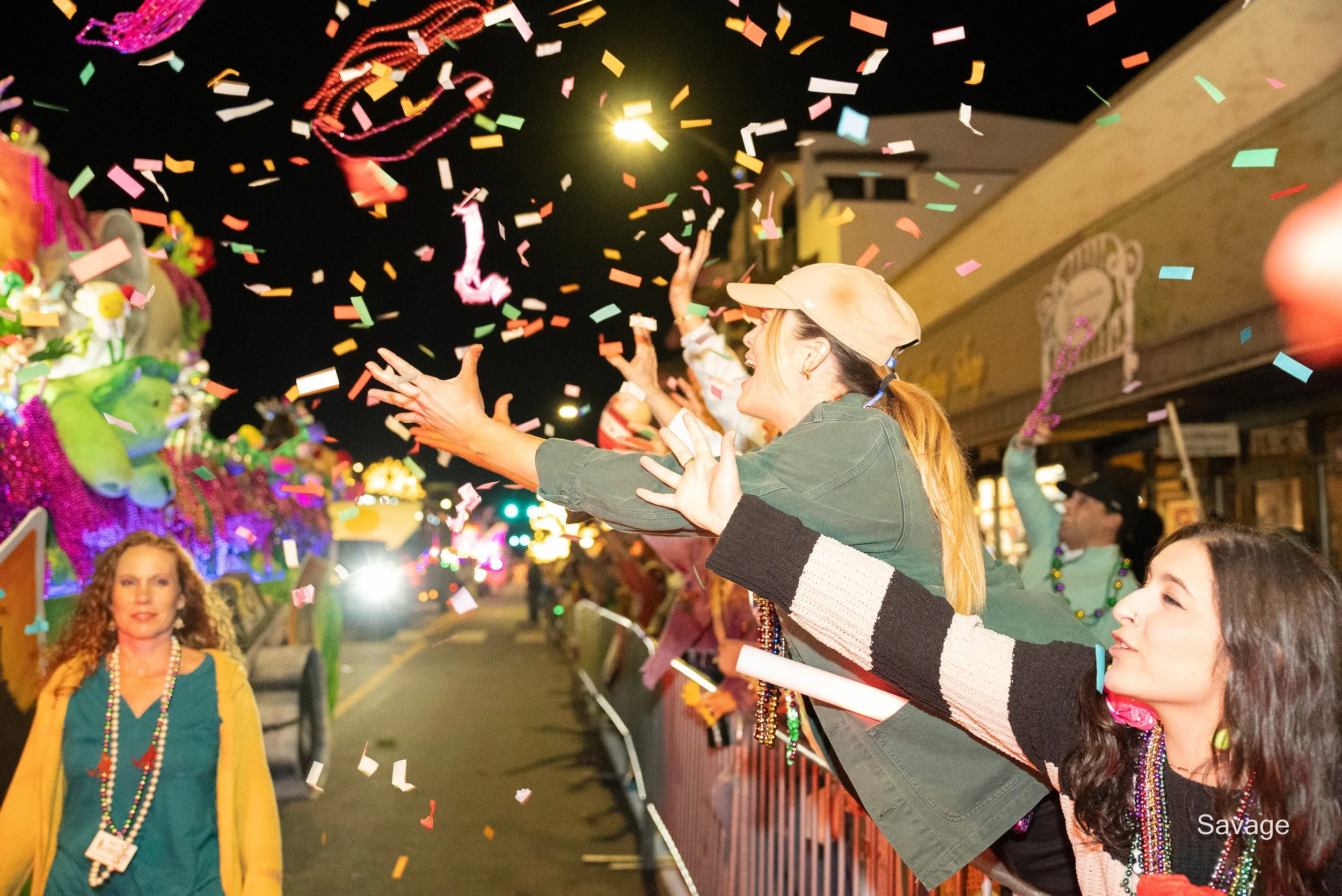 Nighttime parade with people grabbing beads and colorful confetti falling.