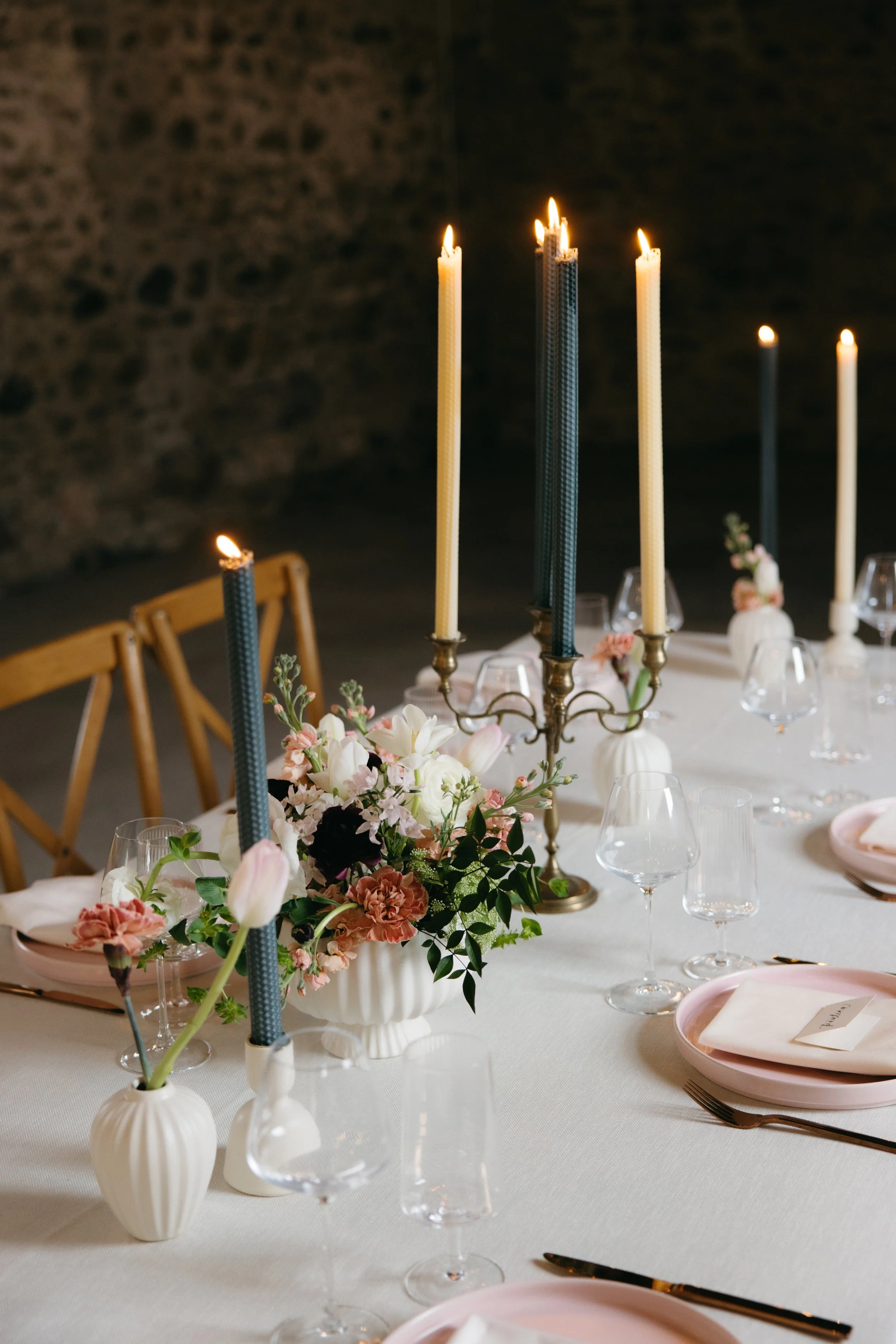 A sophisticated outdoor table setting featuring a crisp white tablecloth, gold flatware, and signature tall beeswax candlesticks for a luxury event.