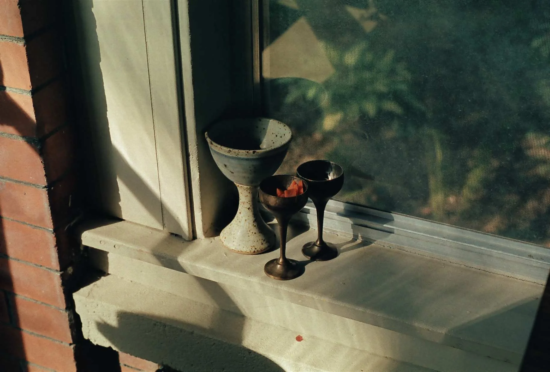 Three goblets on a windowsill; one ceramic, two metallic with one containing small orange items in studio free folk.