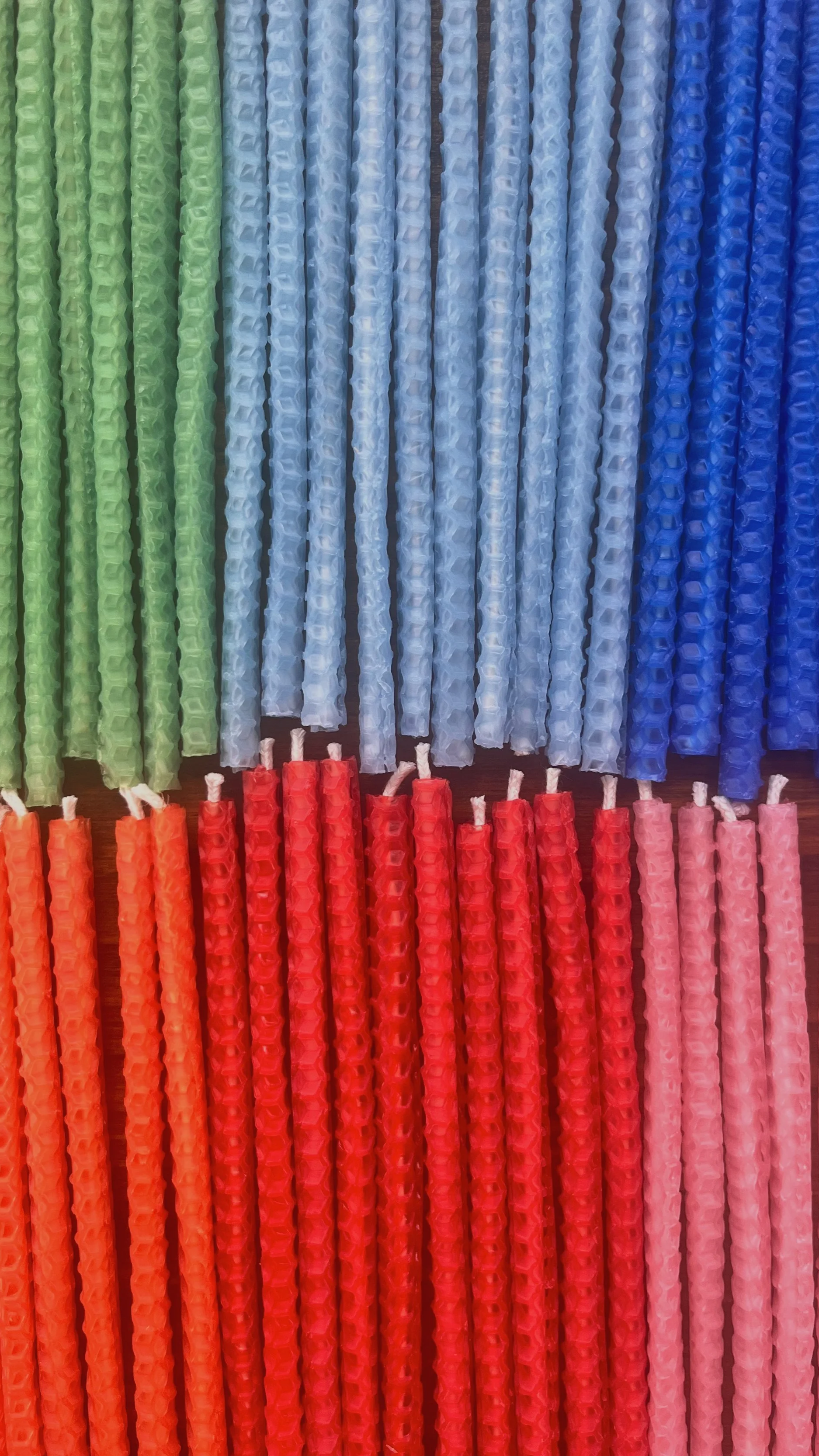 Colorful rolled honeycomb beeswax thin taper candles arranged side by side in blocks of green, light blue, dark blue, orange, red, and pink