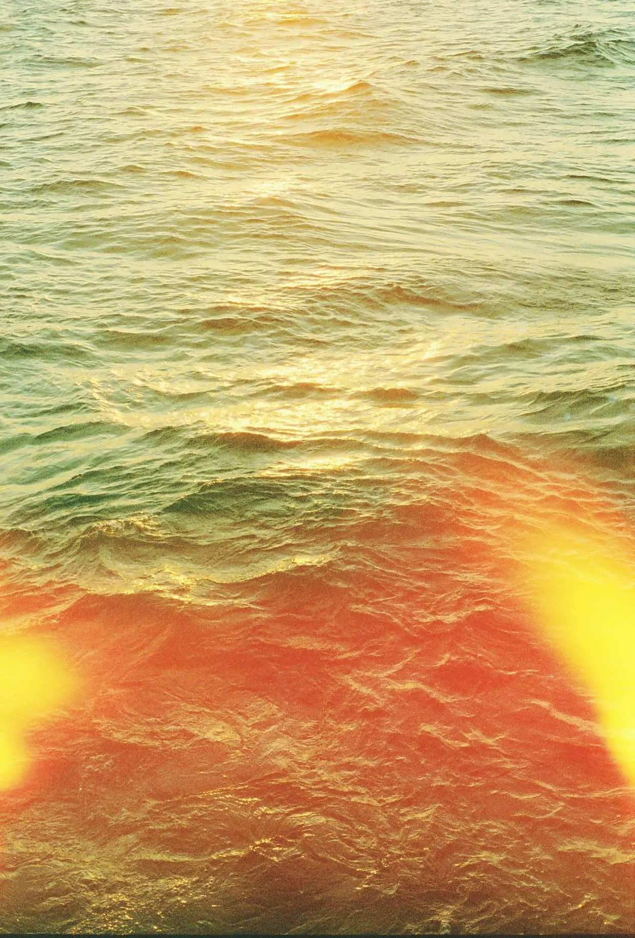 Sunset over ocean with red and yellow light effects on water surface.