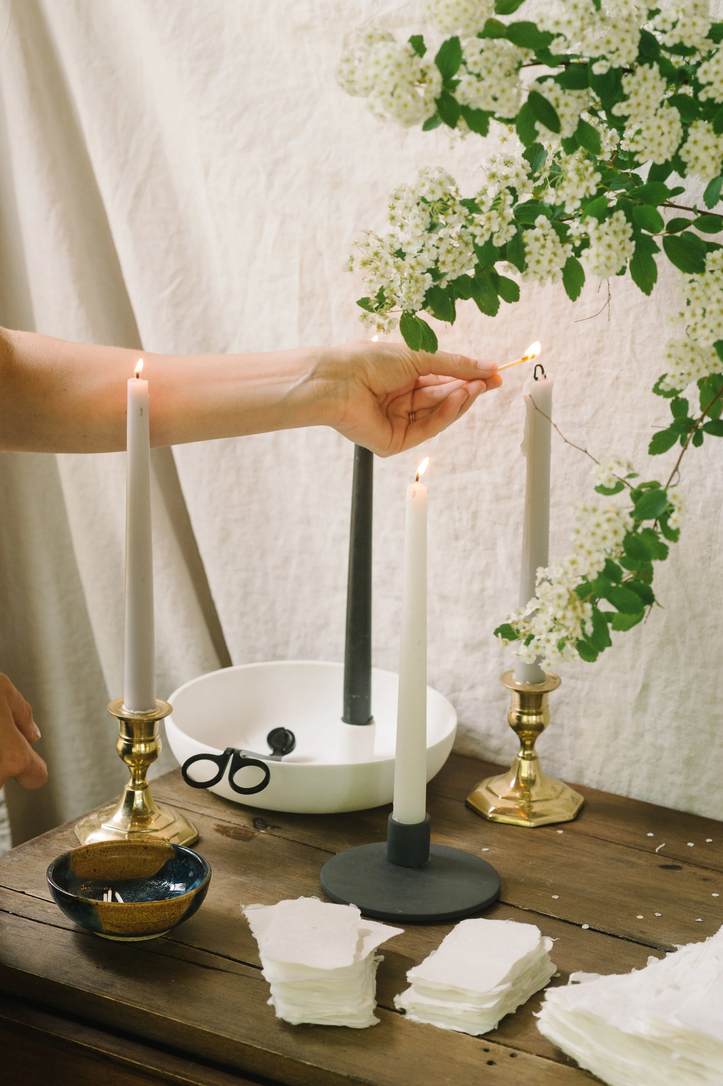 studio free folk beeswax tapers in brass holders being lit next to floral arrangements.
