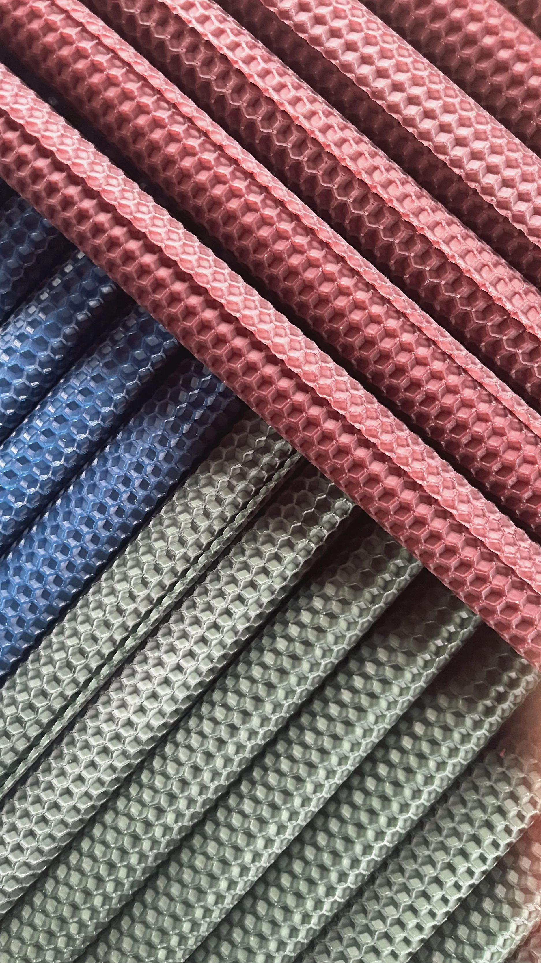 Close-up overhead shot of stacked hand-rolled honeycomb beeswax taper candles in deep red, blue, and sage green arranged in geometric diagonal lines.
