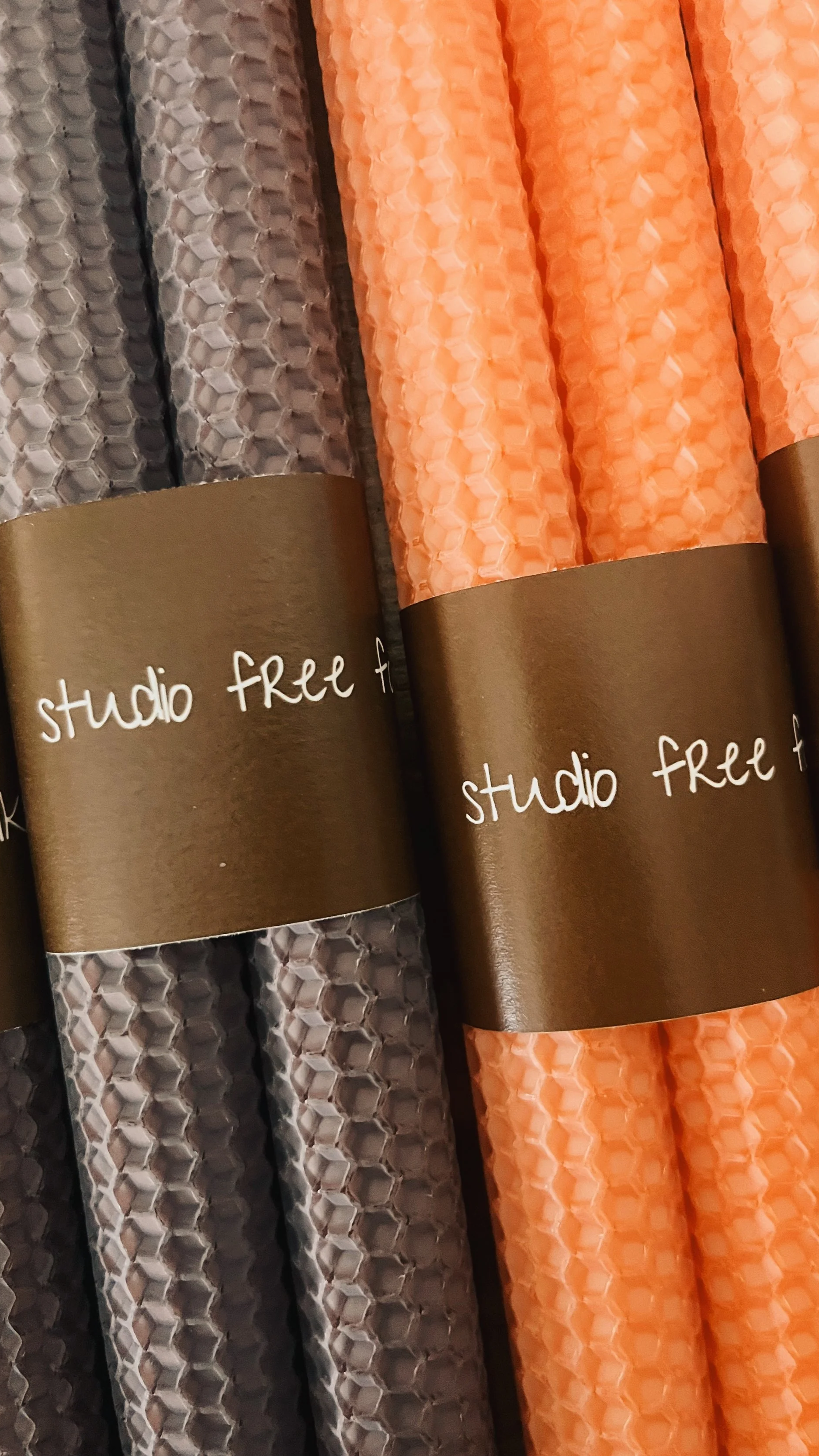 Close-up of pairs of rich brown and soft peach hand-rolled honeycomb beeswax taper candles wrapped in brown paper labels printed with studio free folk.