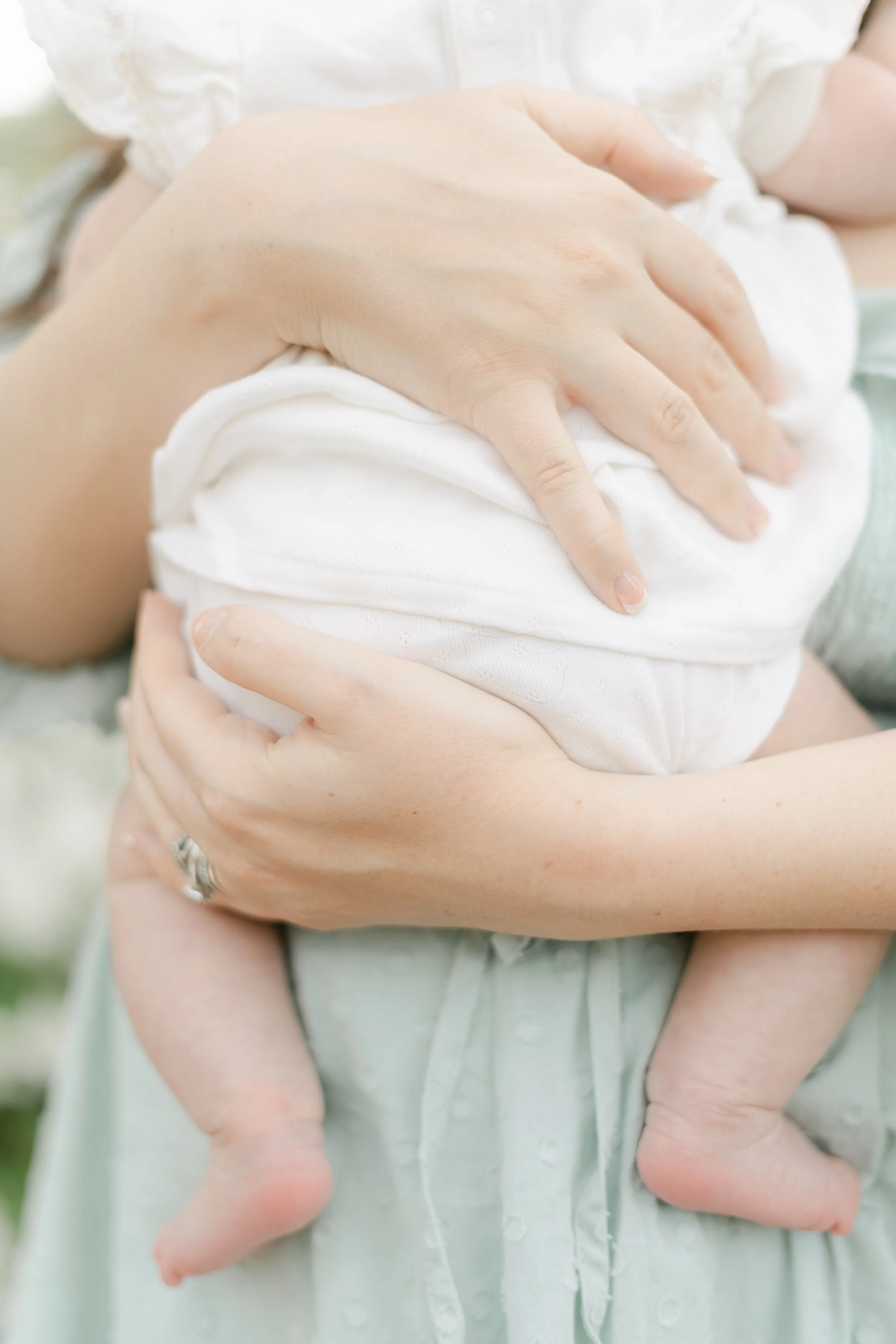 Close-up of a woman holding a sleeping baby, with the baby's head resting on the woman's chest and baby’s legs hanging down.
