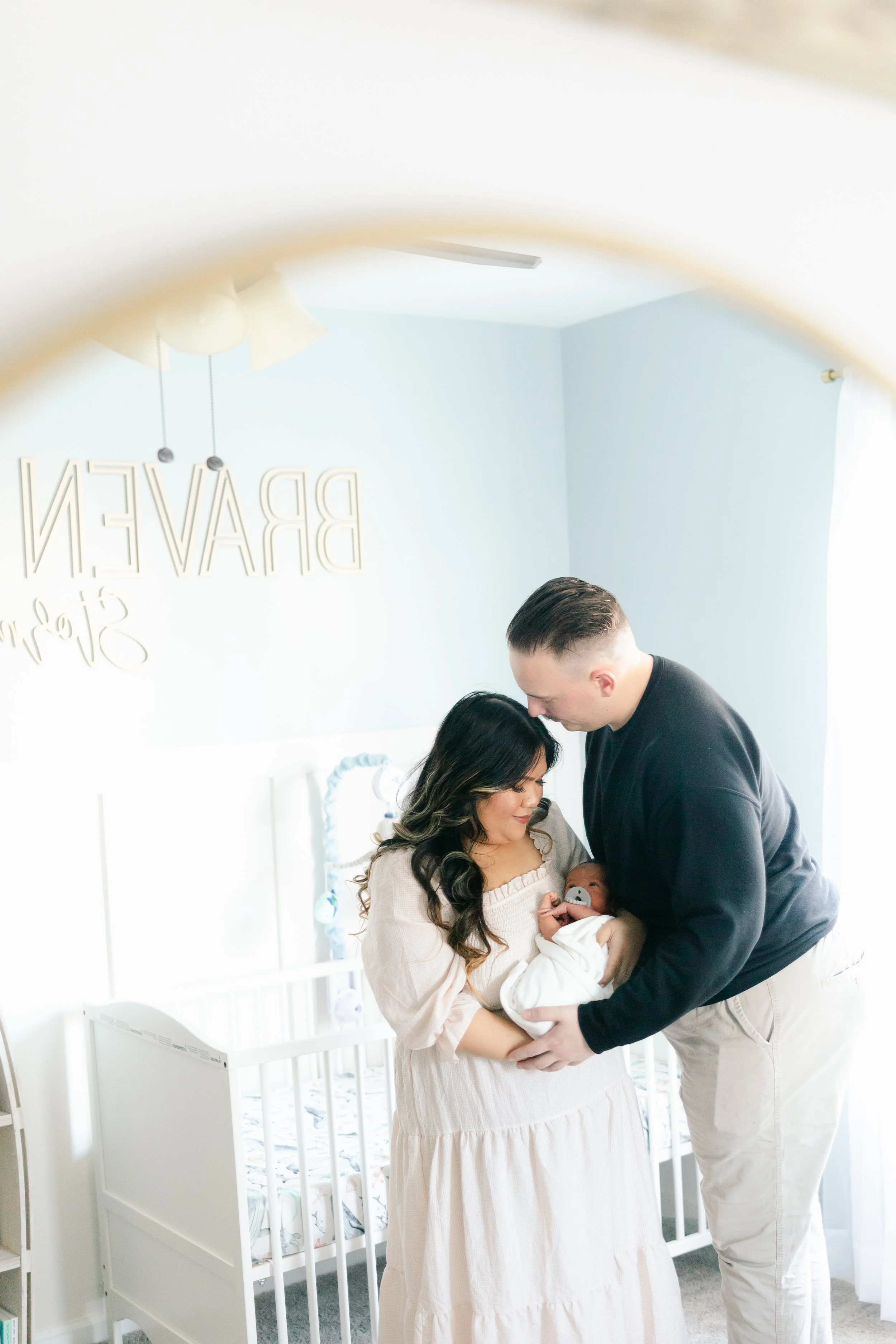 Parents holding a baby in a nursery with a crib and wall decor.