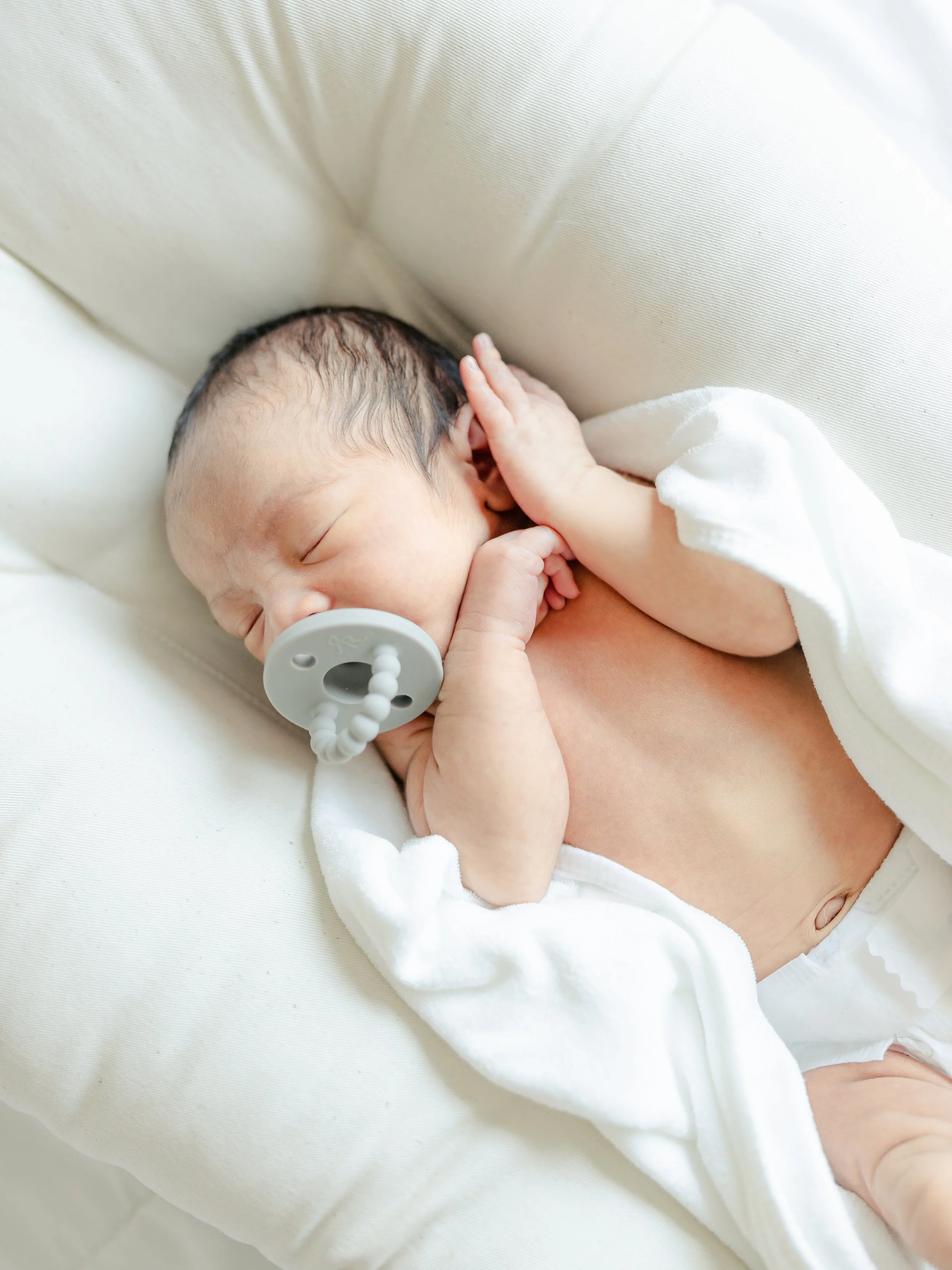 Newborn baby sleeping with a pacifier, wrapped in a white blanket.