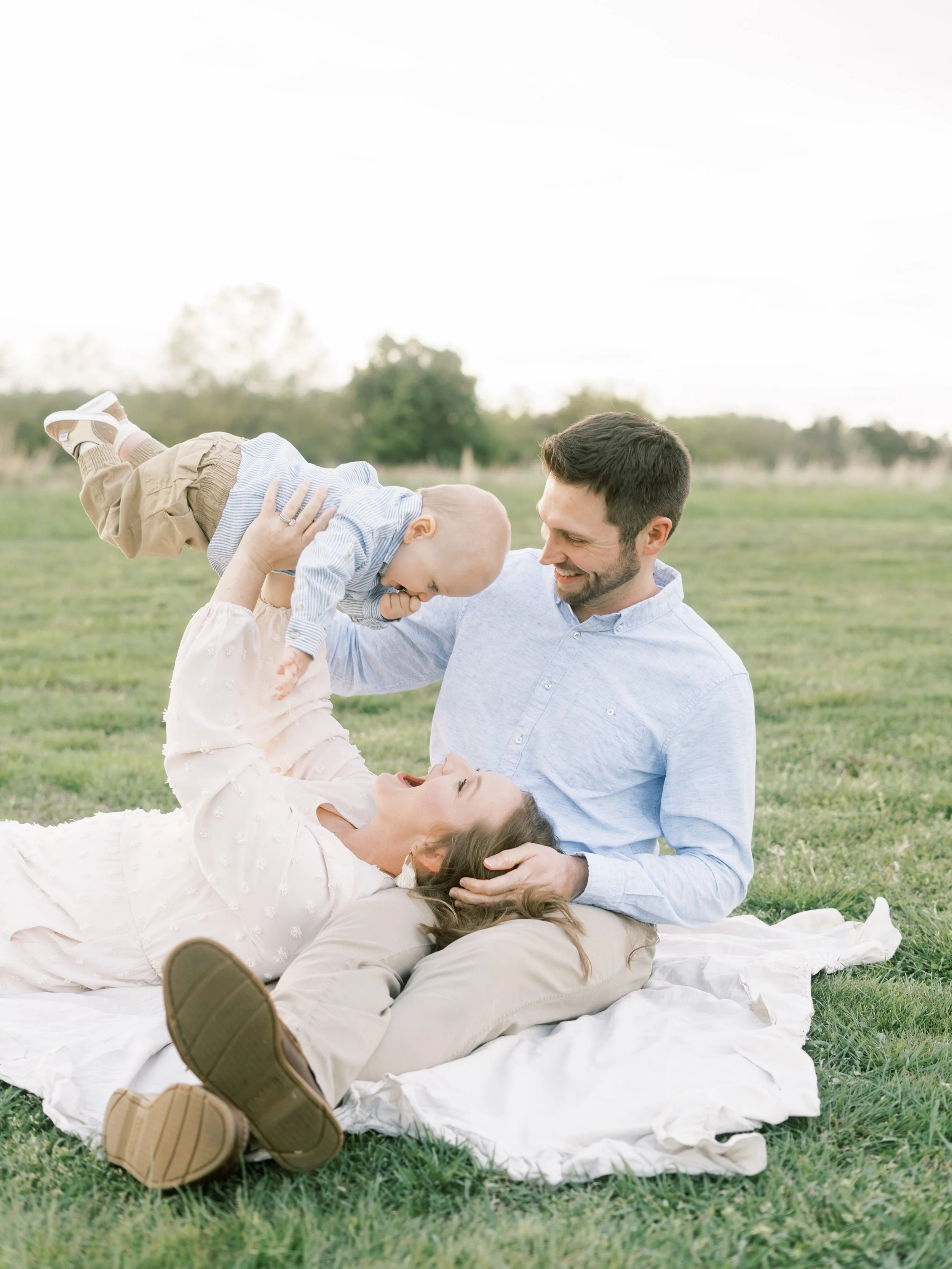 Family of four, two adults and two children, playing and smiling in a grassy field outdoors during daytime in Chesapeake, Virginia