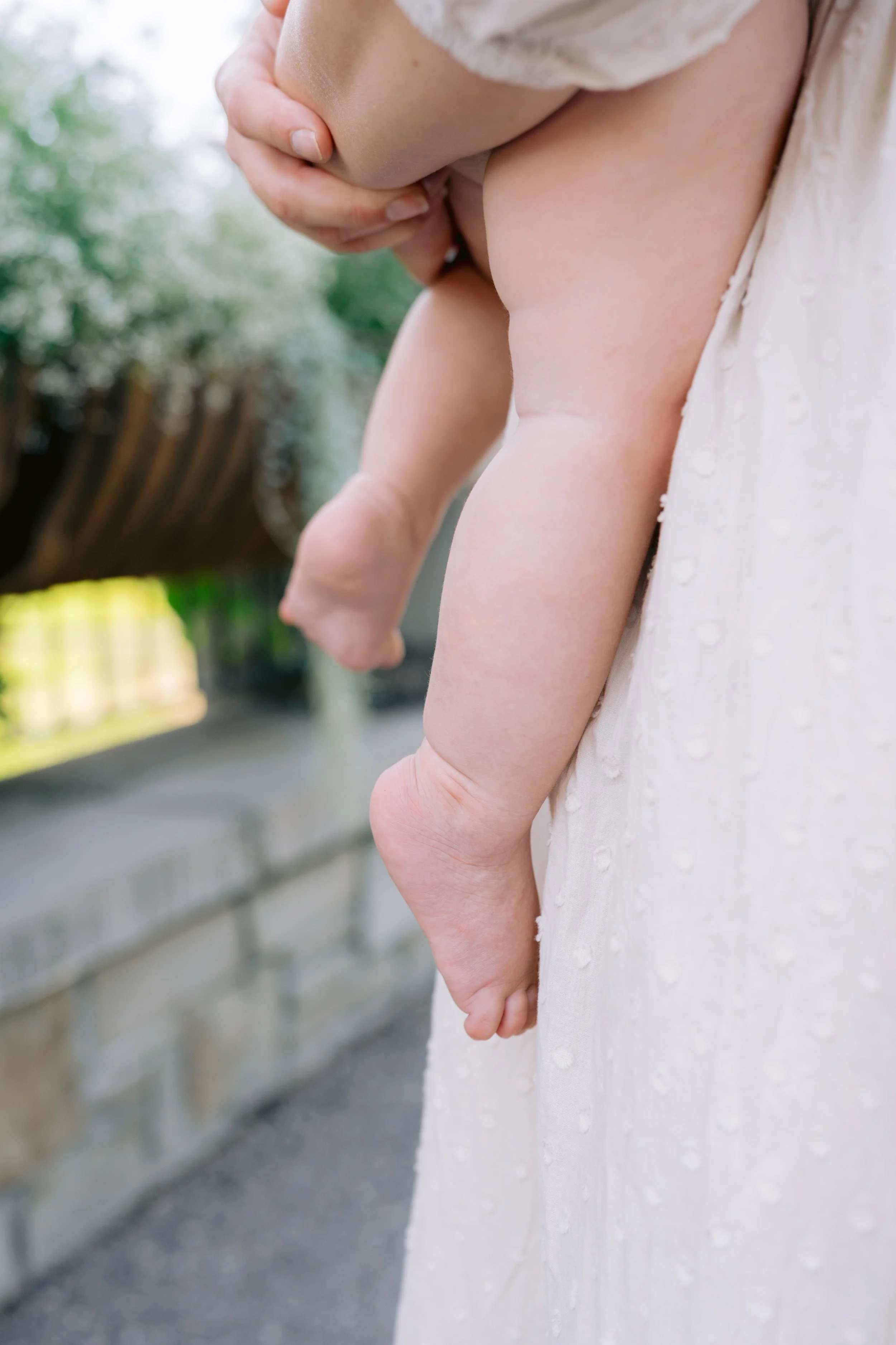 Close-up of a person holding a baby, focusing on the baby's chubby legs and hand.