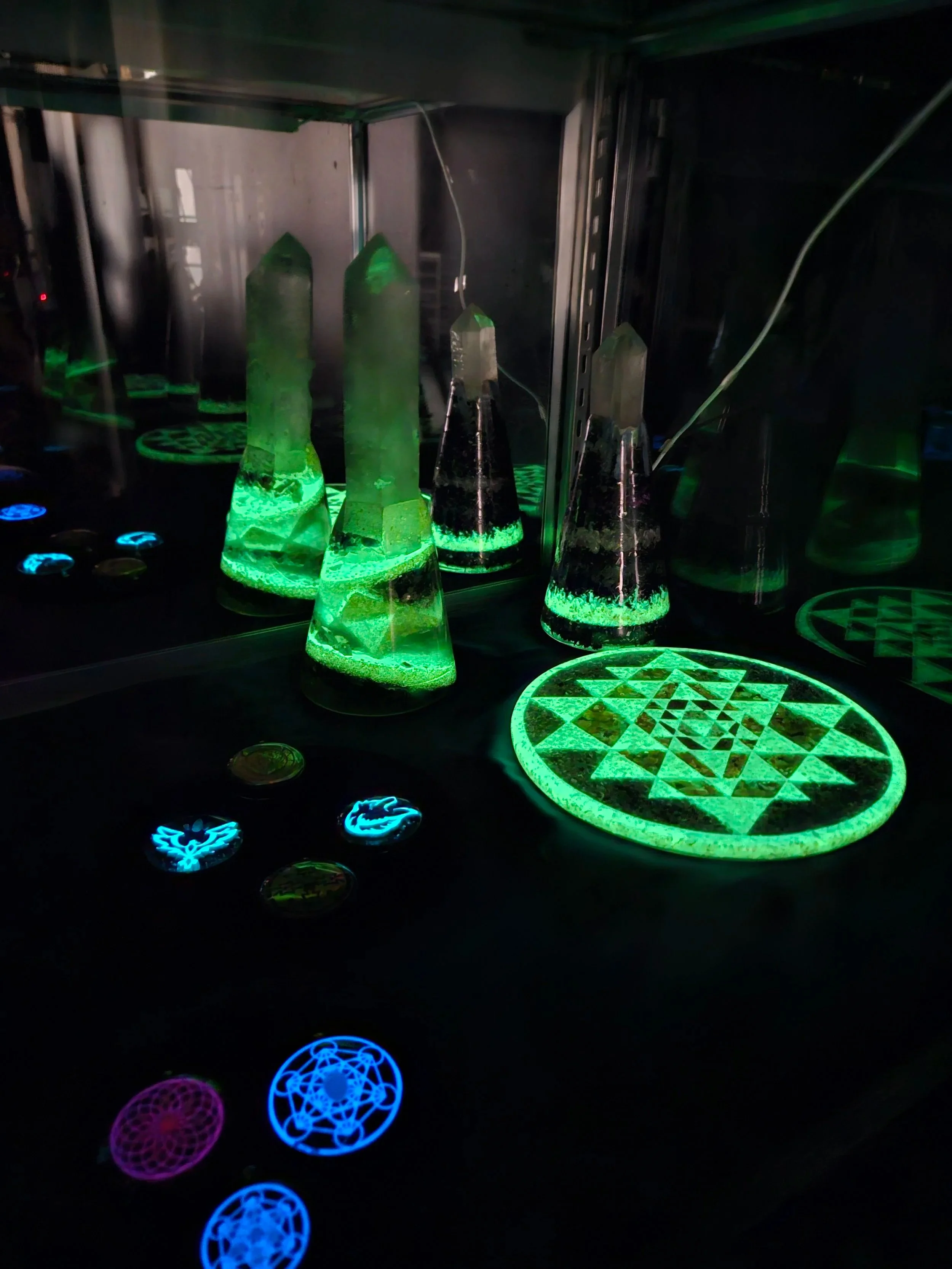 UV cabinet display of glowing orgonite obelisks and Sri Yantra plaque