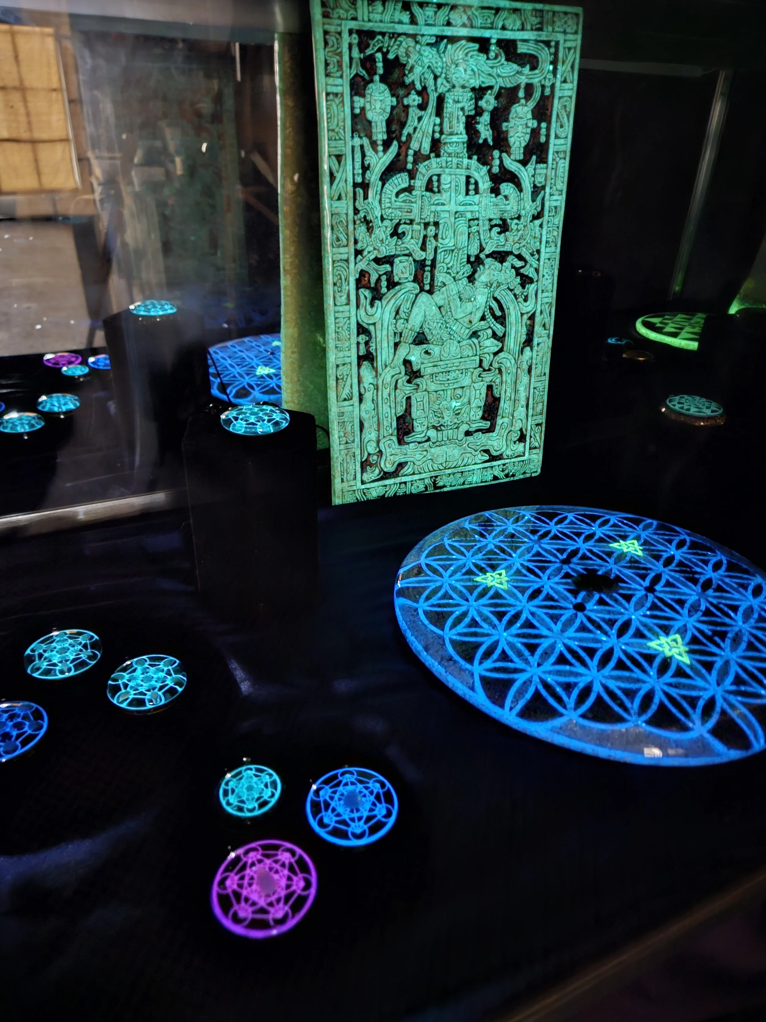 UV-lit Mayan plaque and Flower of Life orgonite pieces in studio cabinet