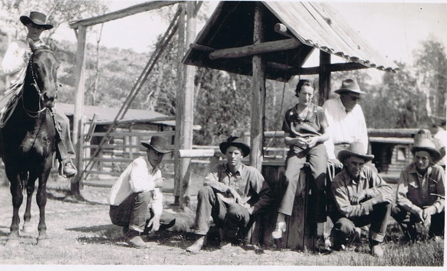 A vintage black-and-white photograph showing six people and a horse. The group consists of four men and one woman, all dressed in old-fashioned clothing. They are gathered around a small shelter, some sitting and some standing. A horse with a rider stands on the left.