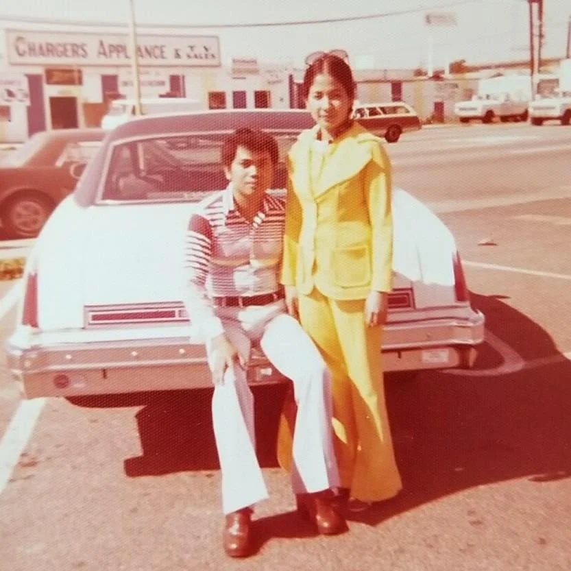 Slim asian man and woman posing in front of car during the 1970s.