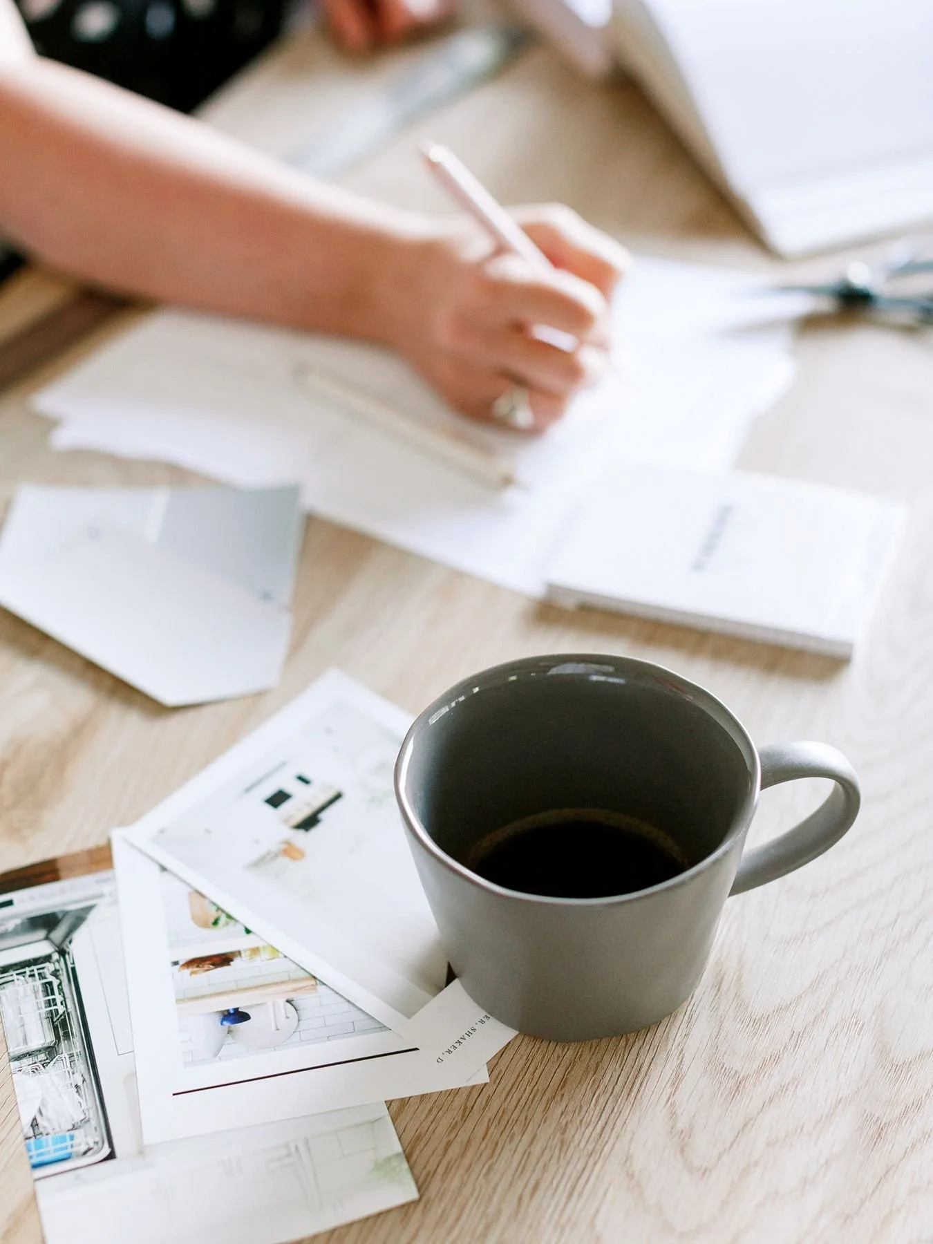 woman's hand seen writing at desk with coffee cup