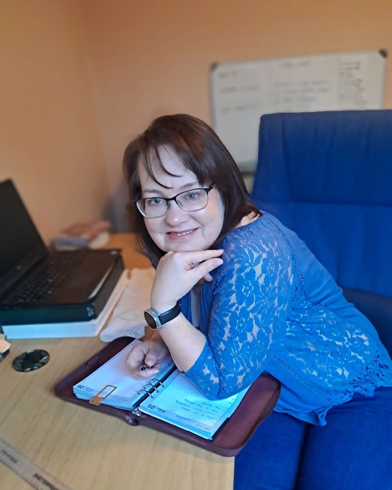 Ronel-sitting-at-desk-leaning-on-hand-with-notebook-and-laptop-visible