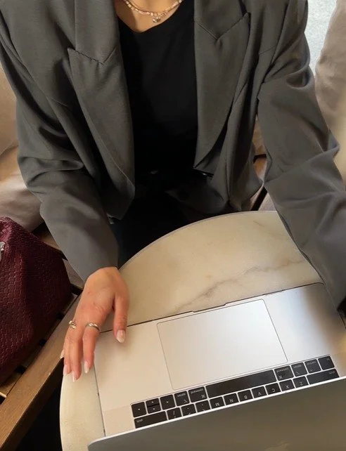 woman in suit sitting at small round table facing laptop