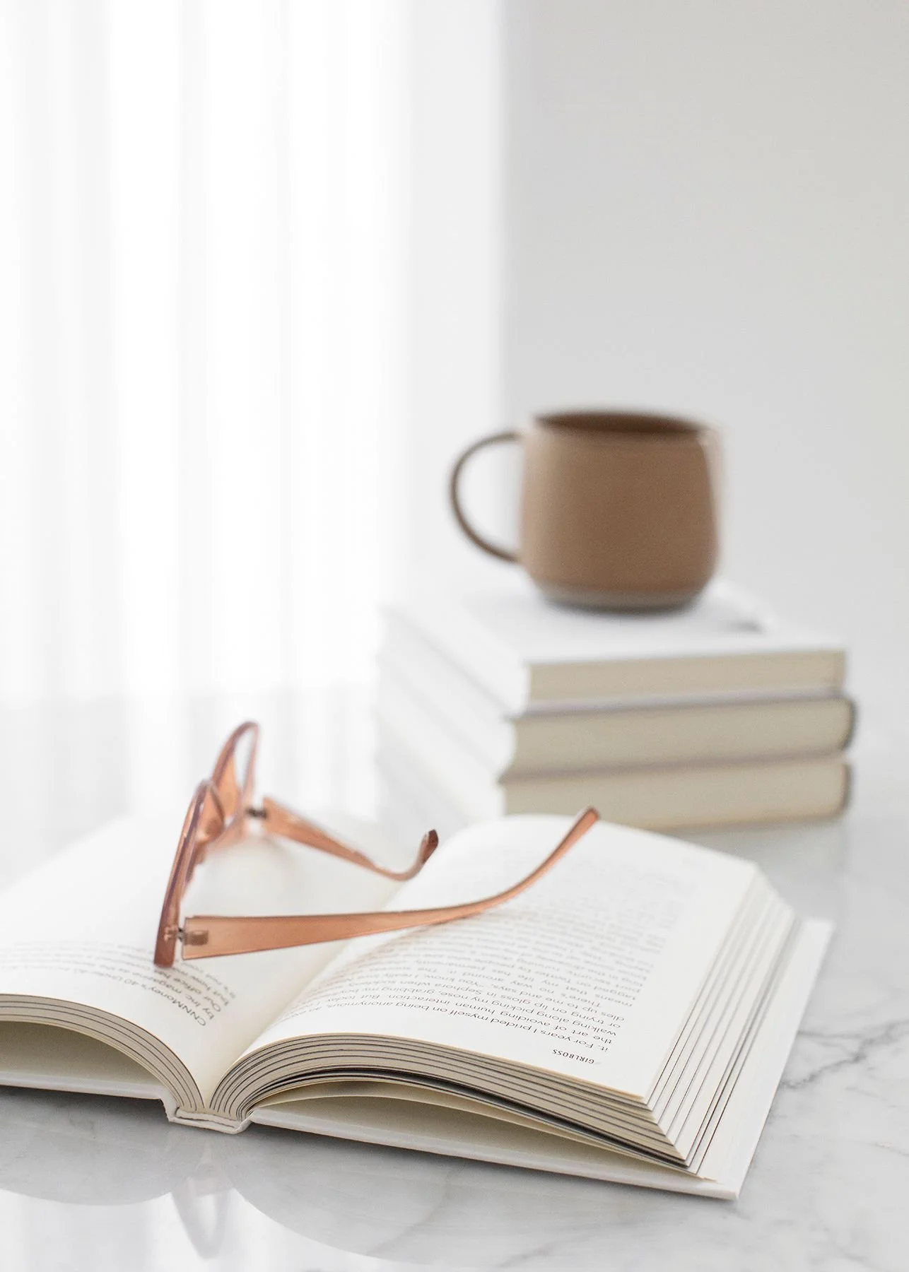 brown-coffee-cup-on-stack-of-book-plus-open-book-with-glasses-on-book