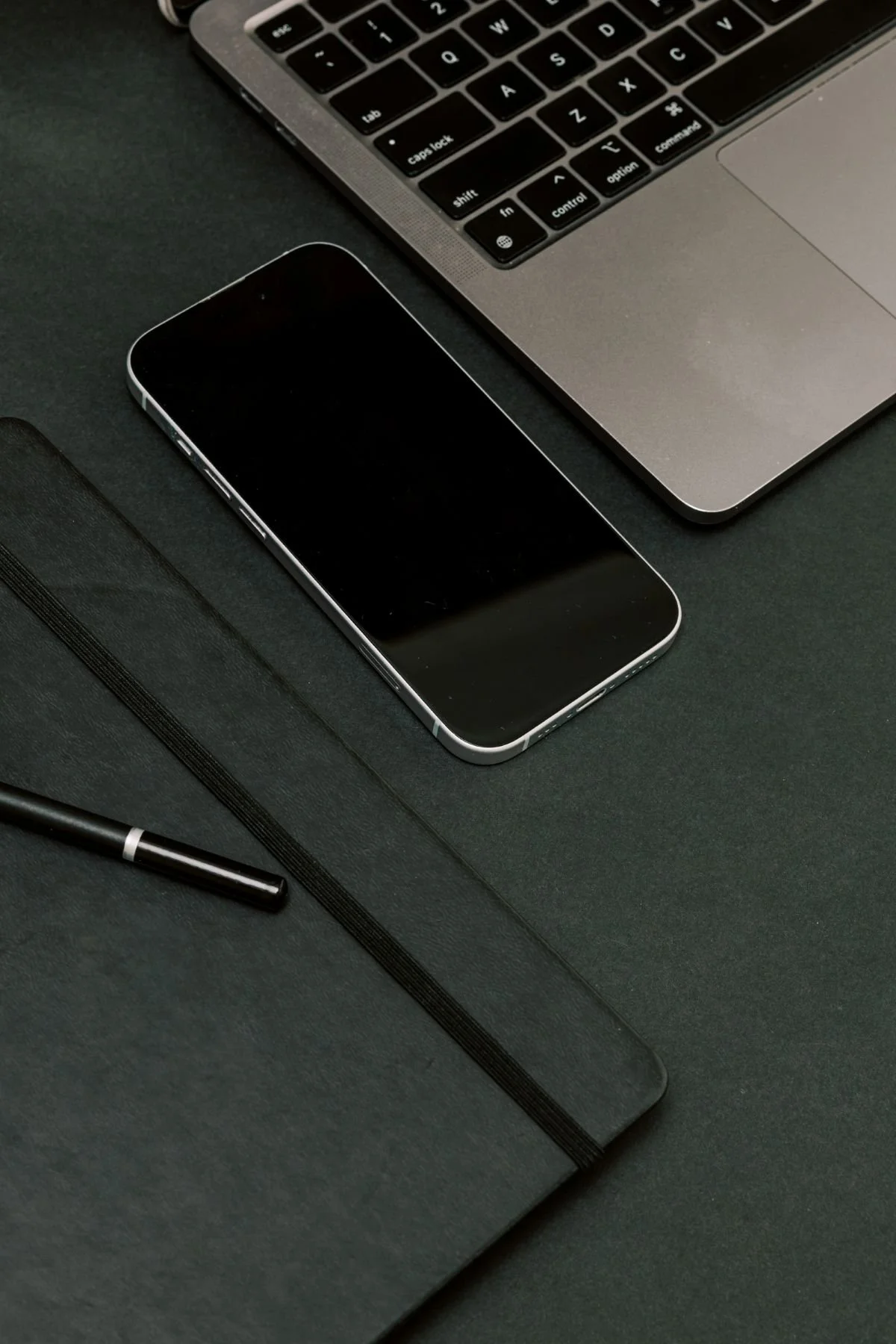 laptop phone and pen on dark desk