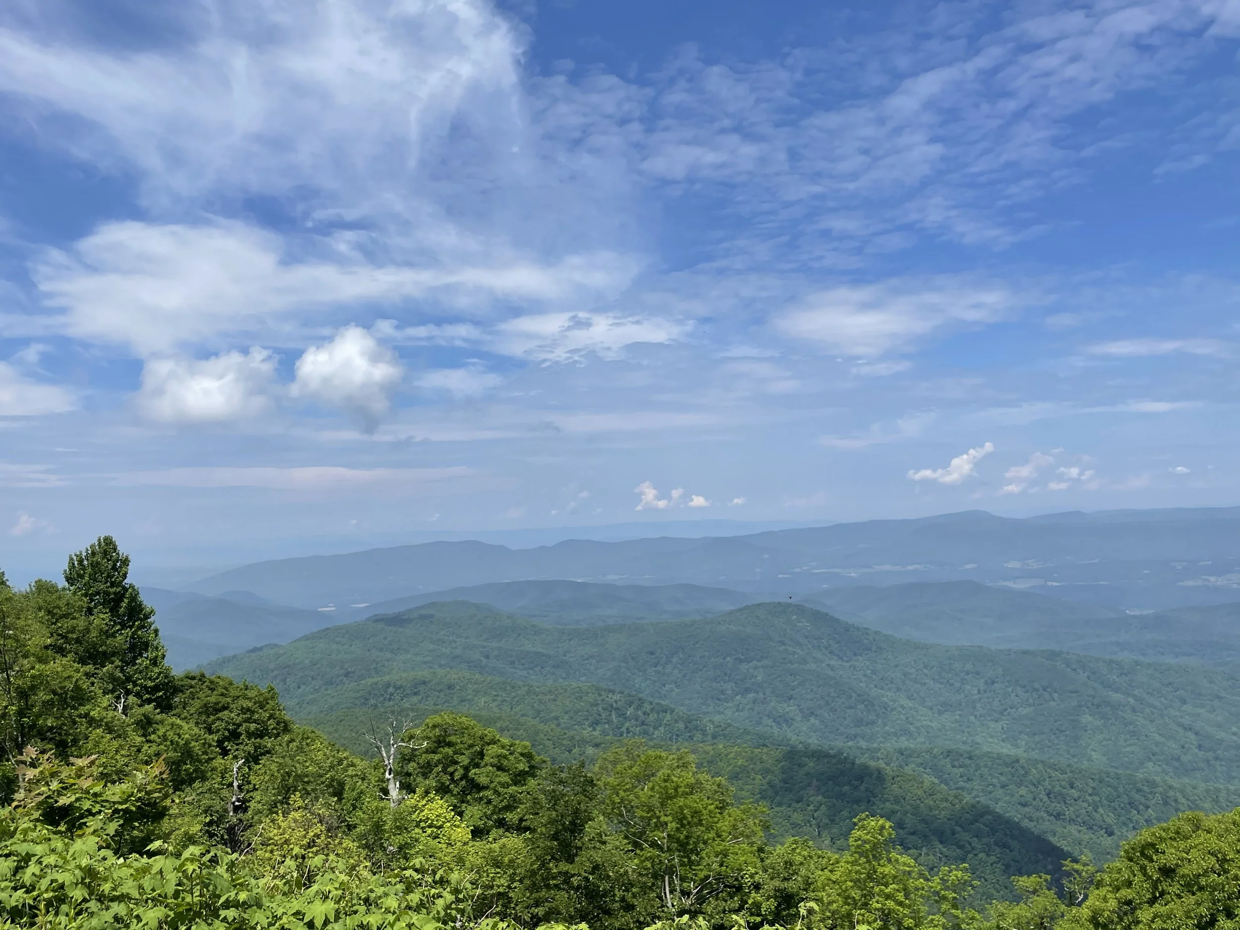 A scenic view of rolling green mountains under a blue sky with wispy white clouds.
