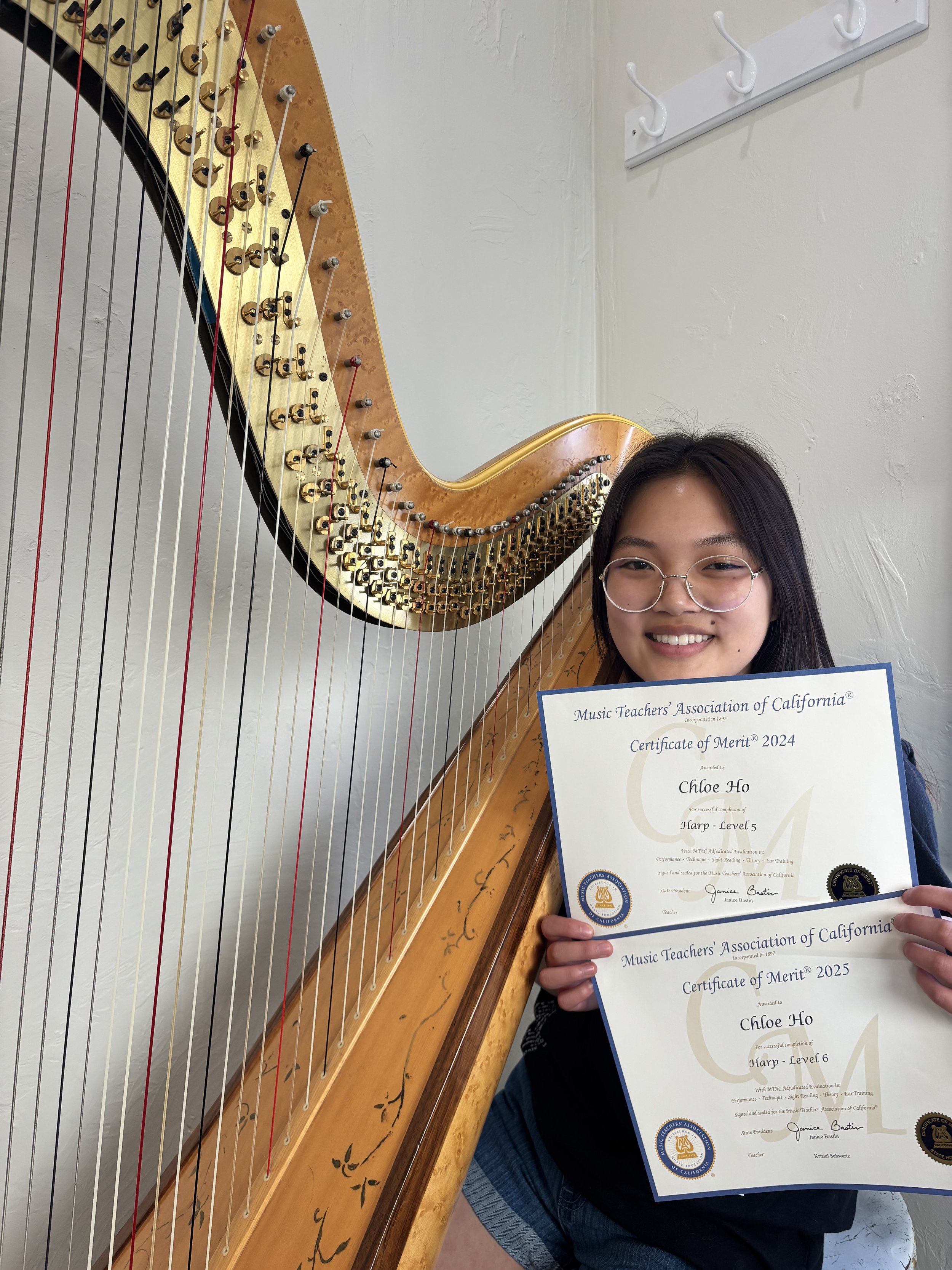 Person holding two certificates in front of a harp, smiling.