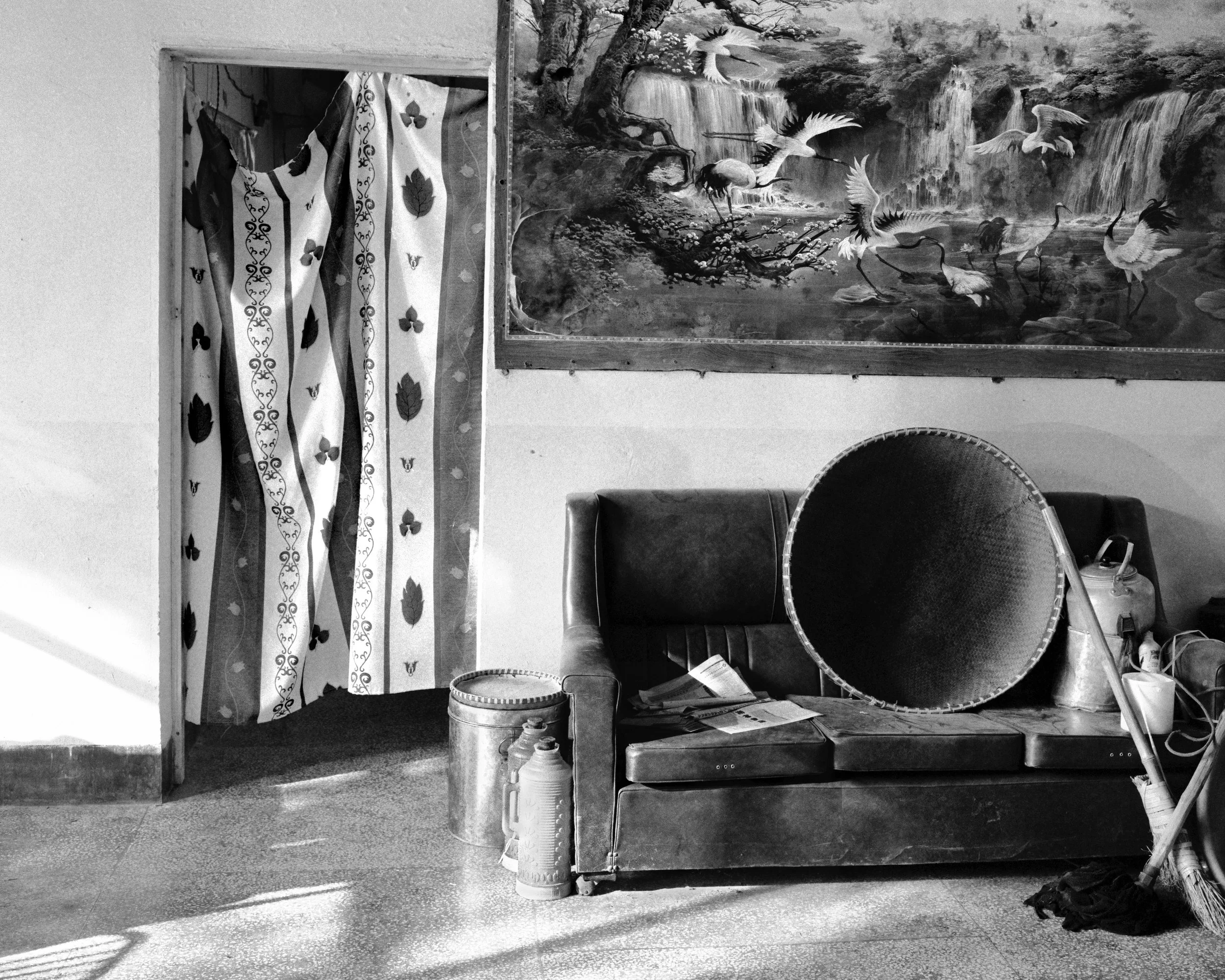 Interior of a tea farmer’s residence in Yunnan Province, 2004, with a well-used sofa, household containers, and a painted wall mural.