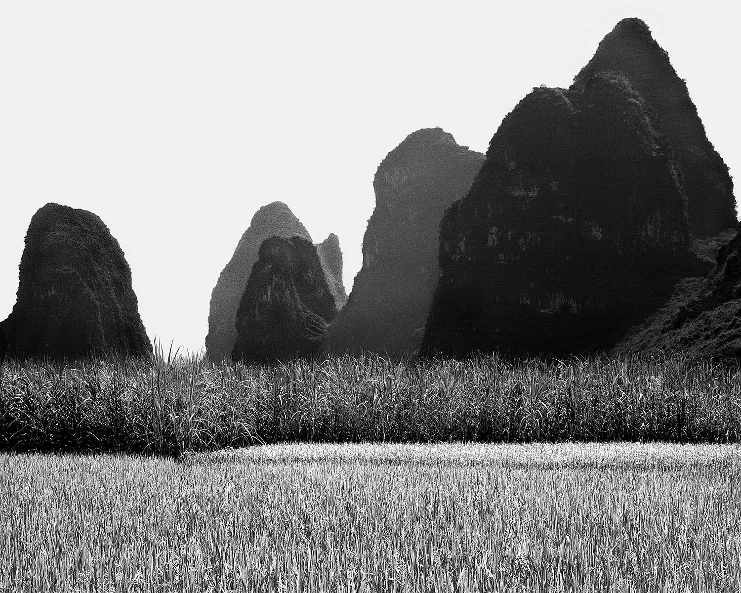 1986, Yangshuo, Guangxi, China: steep karst peaks rise behind cultivated fields, with dark mountain silhouettes against a pale sky.