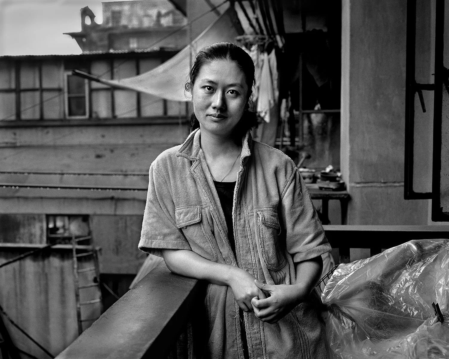1988, Shanghai: Wang Anyi stands on her balcony with one arm resting on the railing, looking toward the camera, with neighboring buildings behind her.