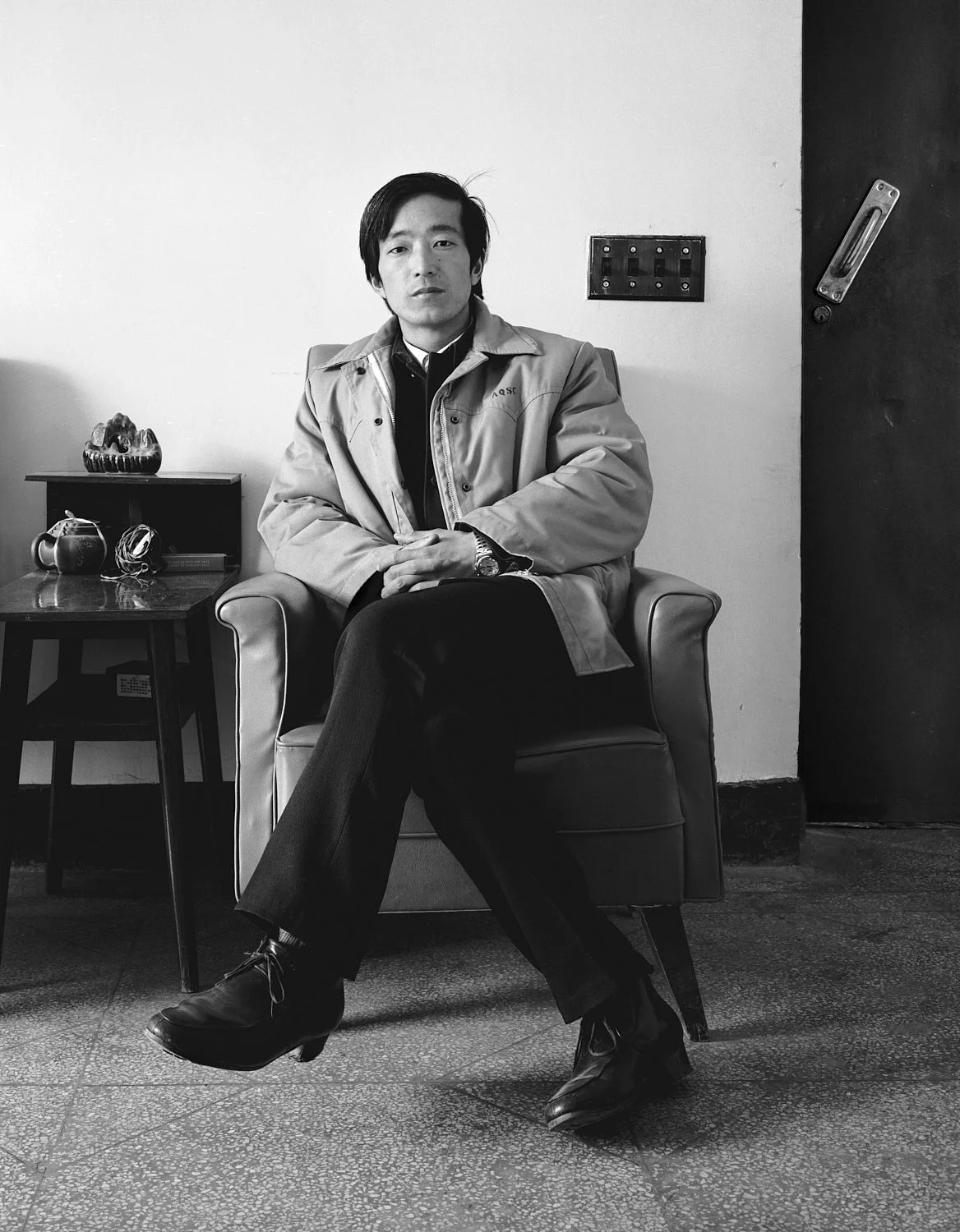 1988, Chongming Island, China: a commune farmer sits in an upholstered armchair with his legs crossed, beside a small table and tea service.