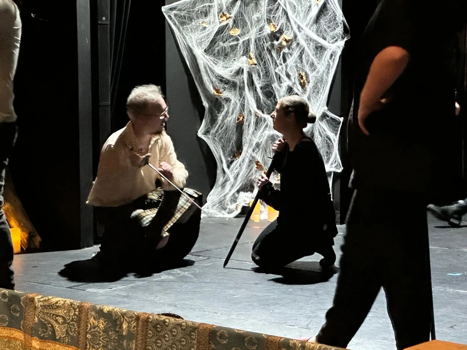 Edge of stage, decorated with spiderwebs. Fight call for Macbeth, Maria and Nate crouched with swords, discussing choreography.